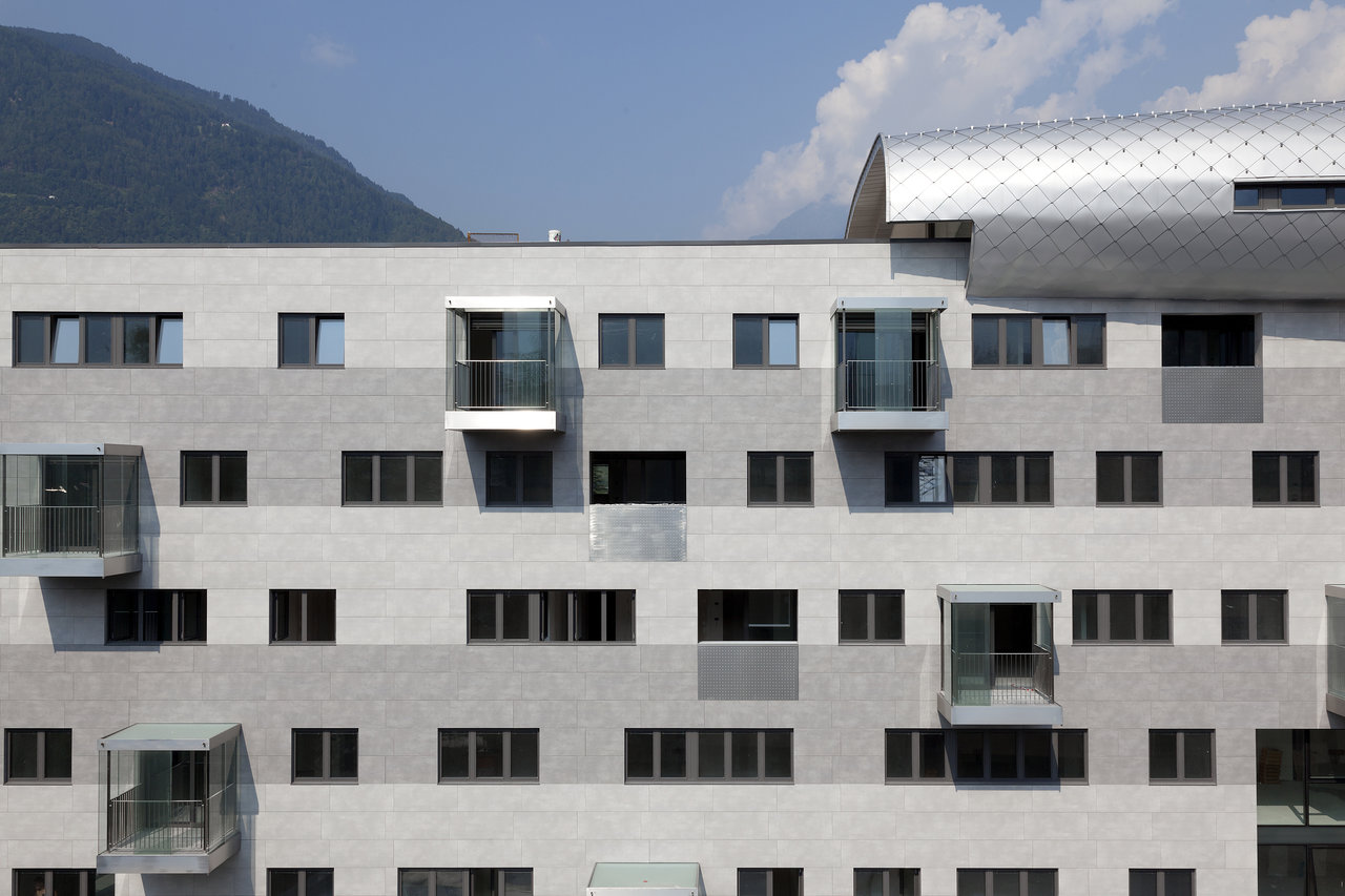 Modern facade with light and dark grey tiles, windows, and glass balconies.