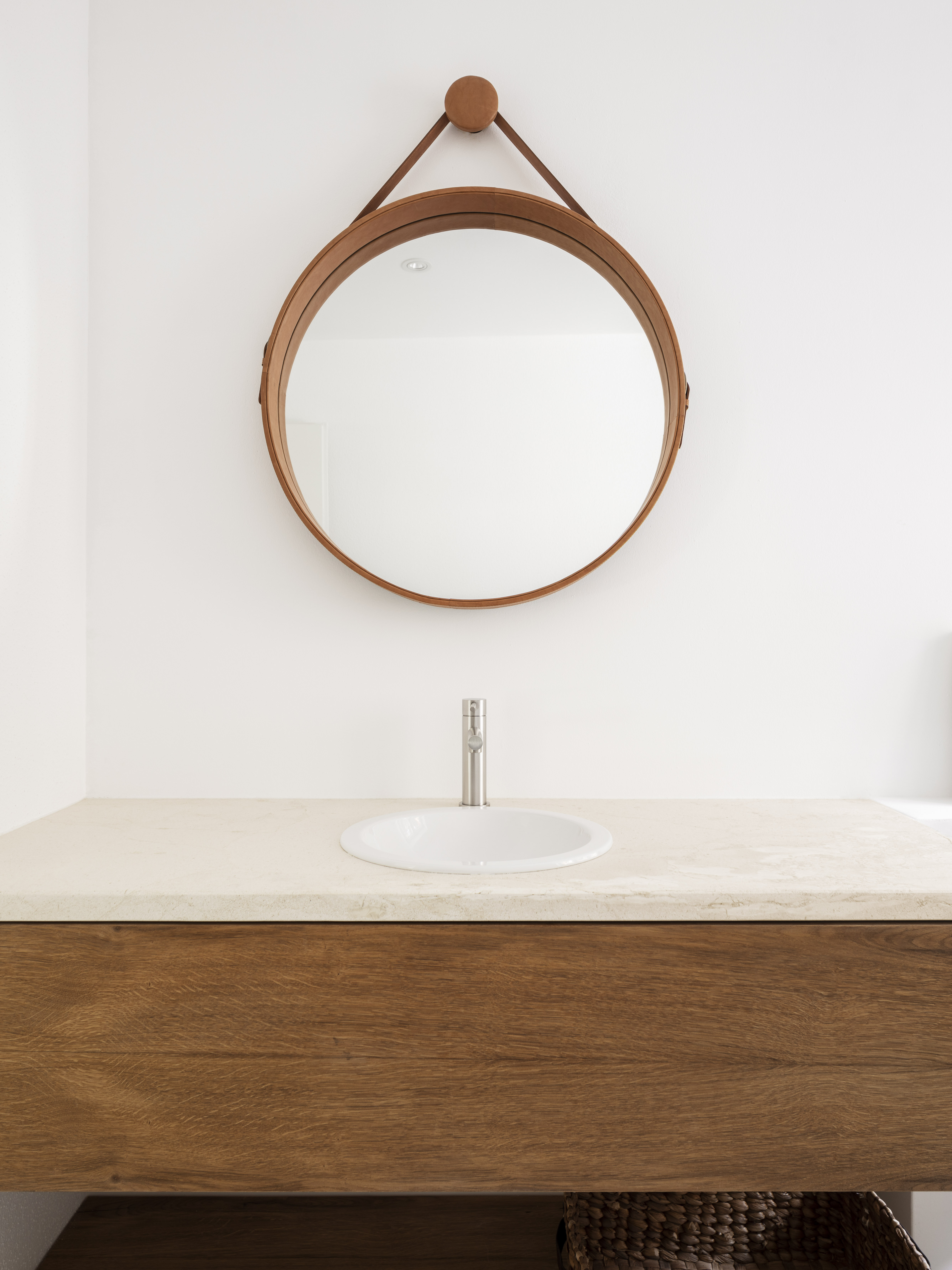 Modern bathroom with wooden vanity, sink, and round wooden mirror.