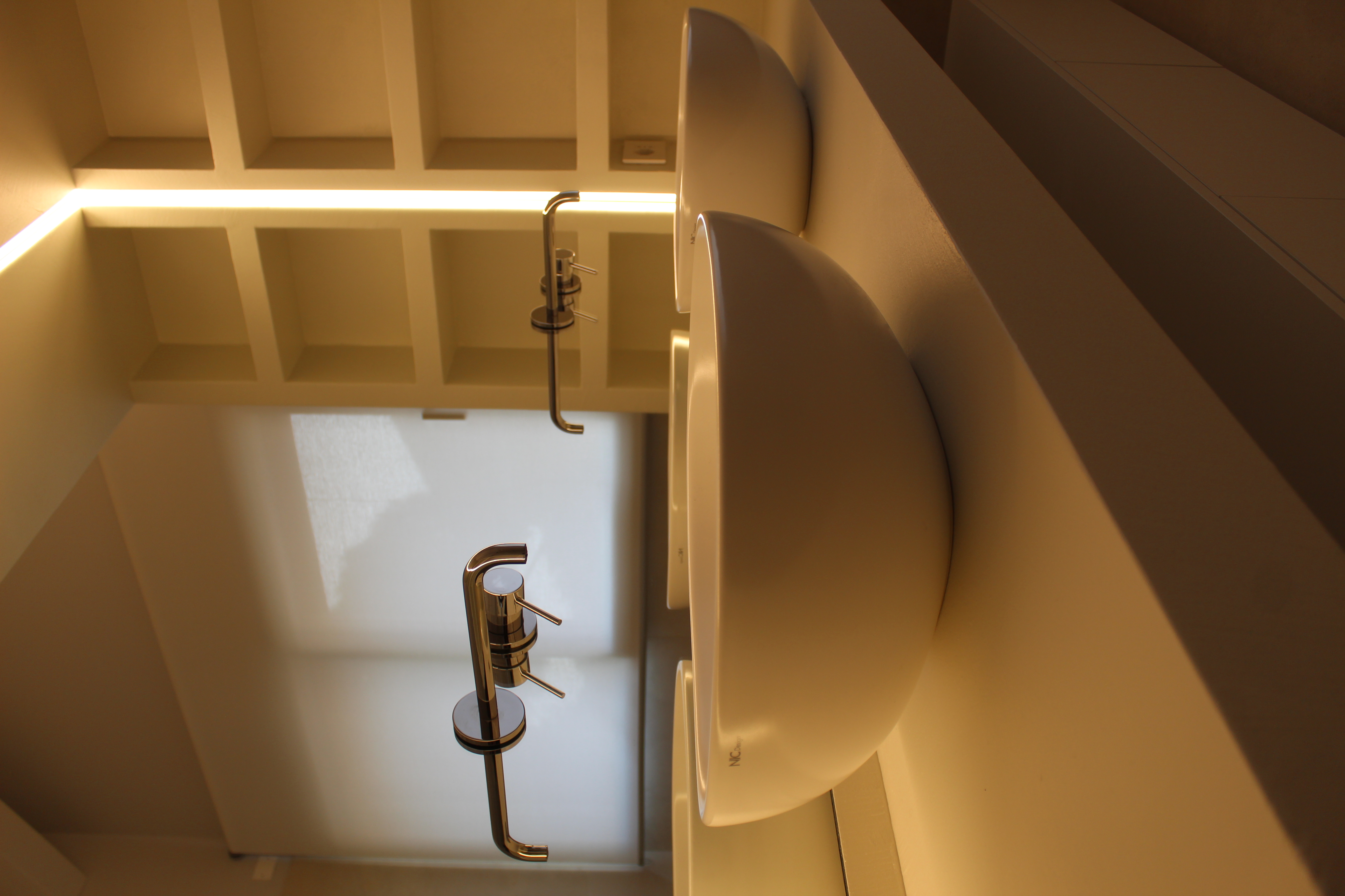 Modern bathroom with white countertop basins, elegant taps, and indirect lighting.