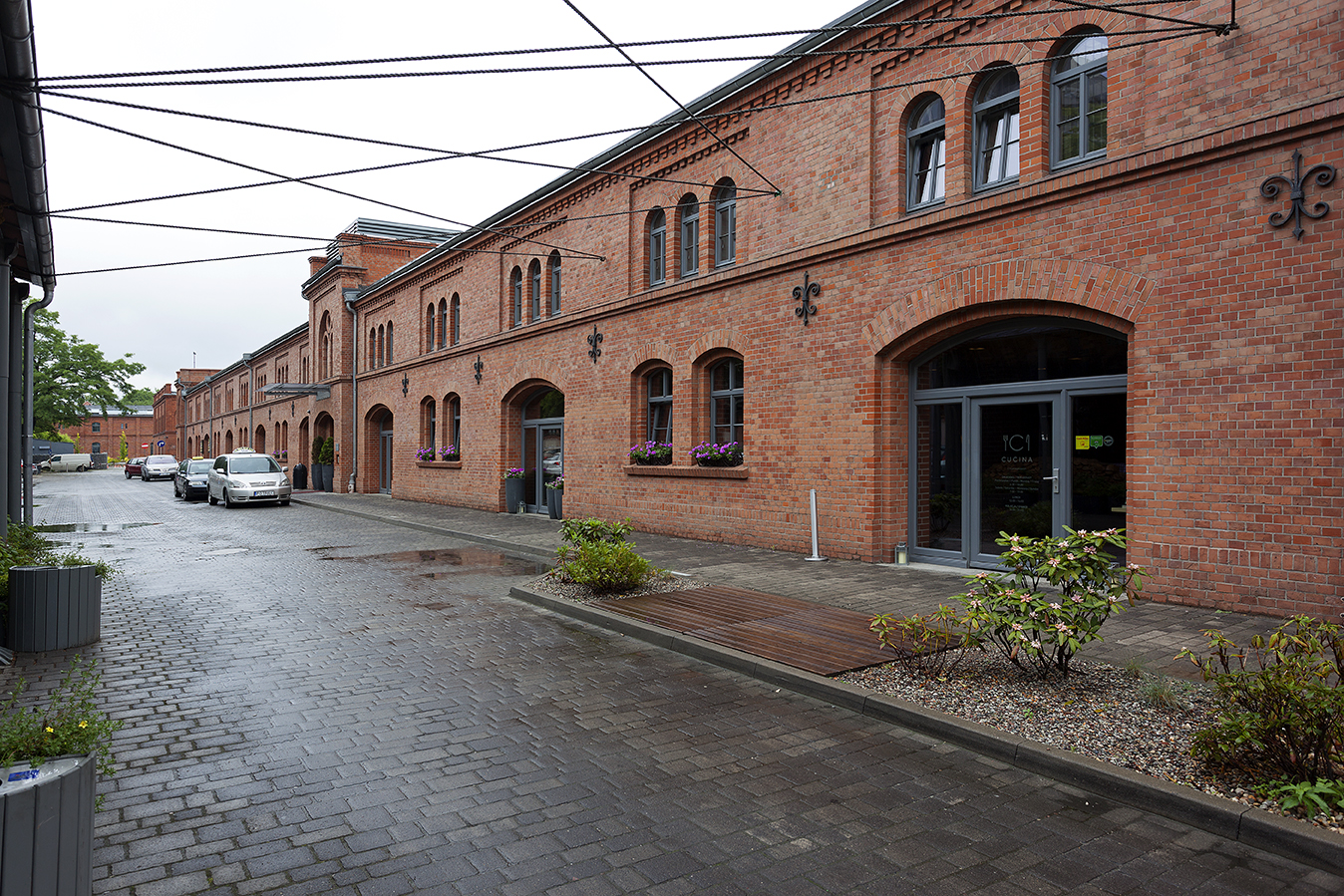 Historic brick building with large arched windows and wet cobblestone street.