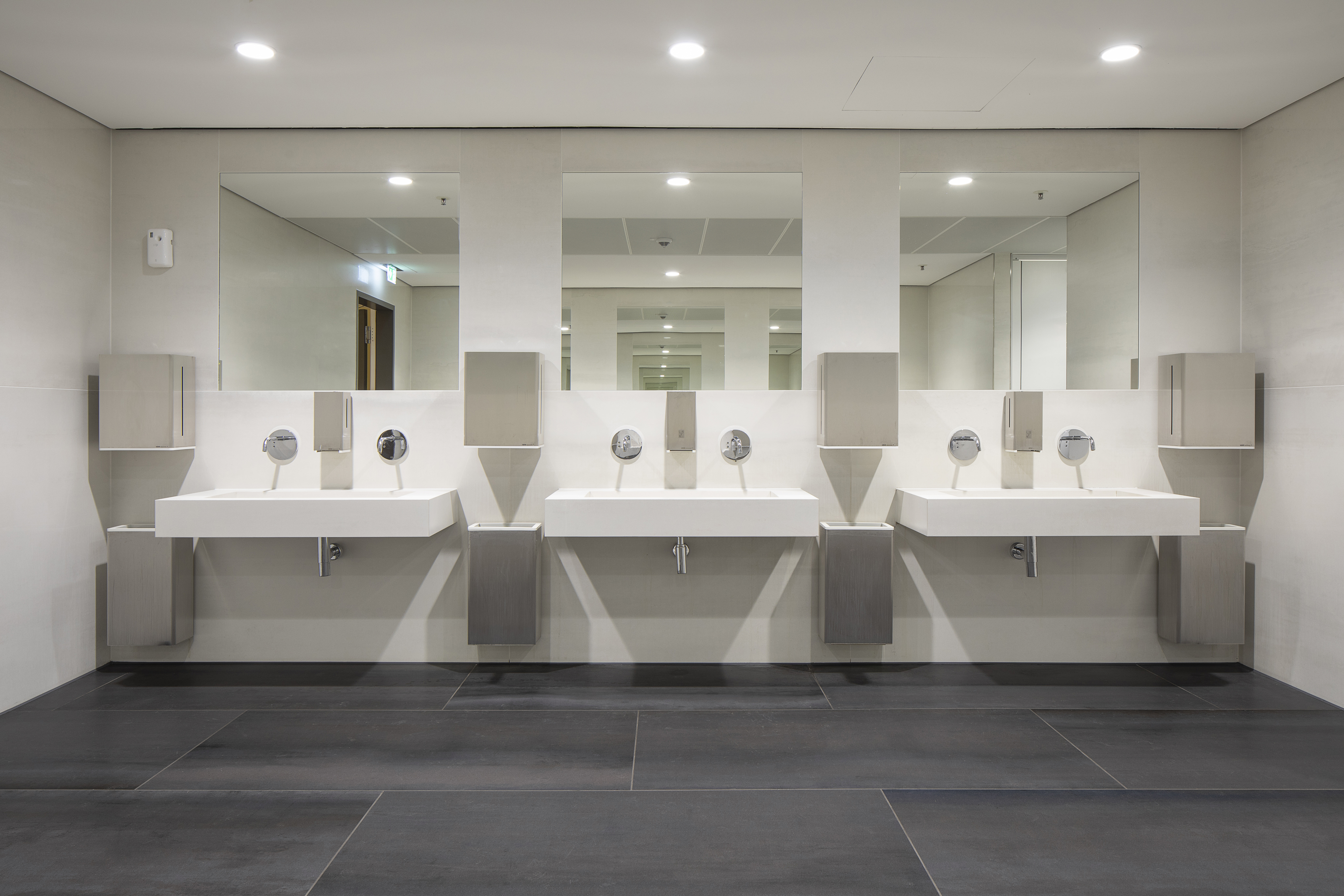 Modern washroom design with dark floor tiles and three stylish sinks.