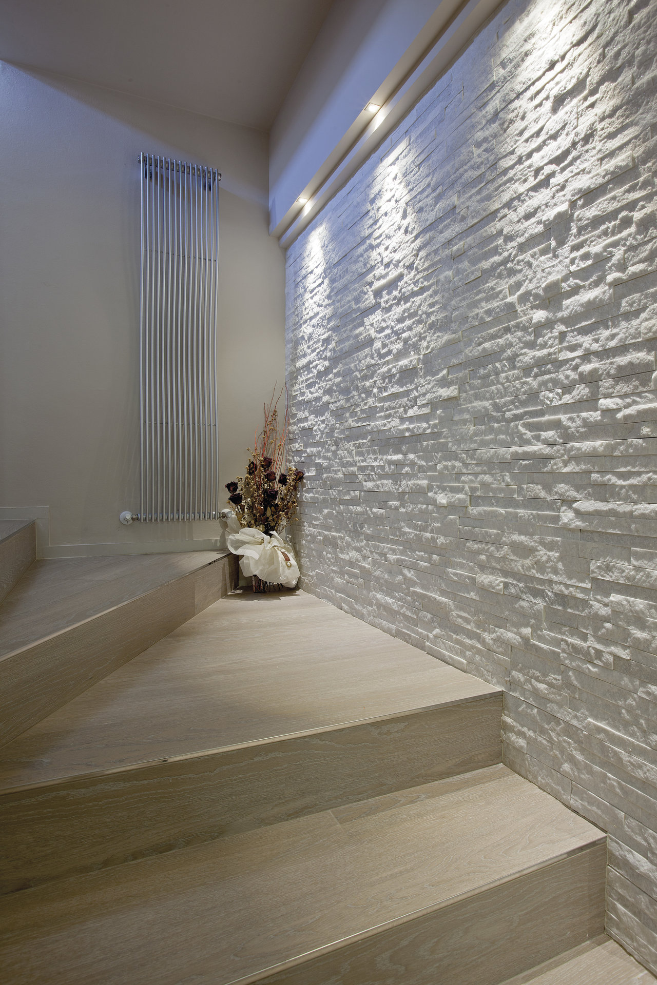 Modern staircase with wood-look tiles and a white stone-look accent wall.