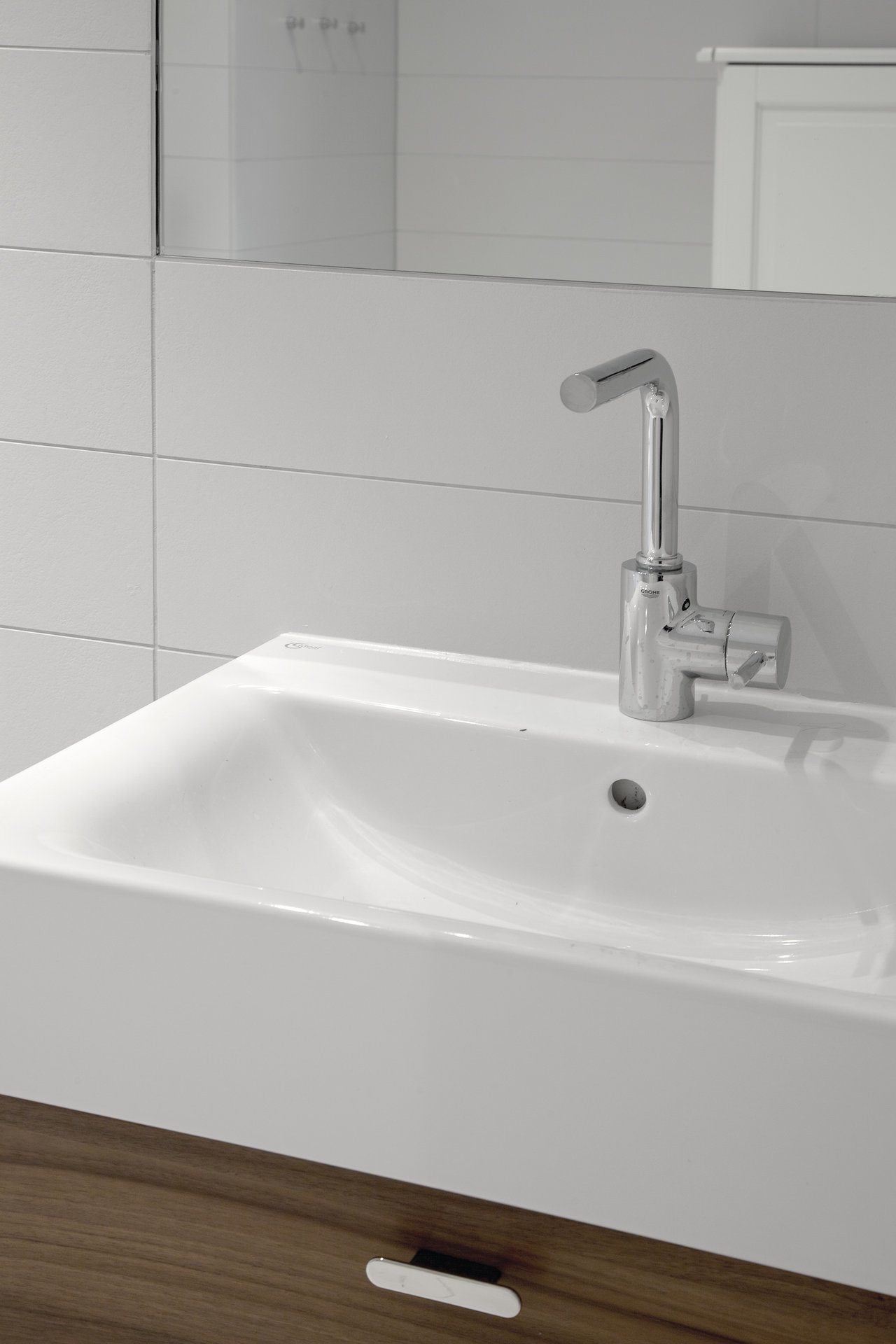 Light wall tiles in a modern bathroom above a washbasin with a wooden vanity unit.