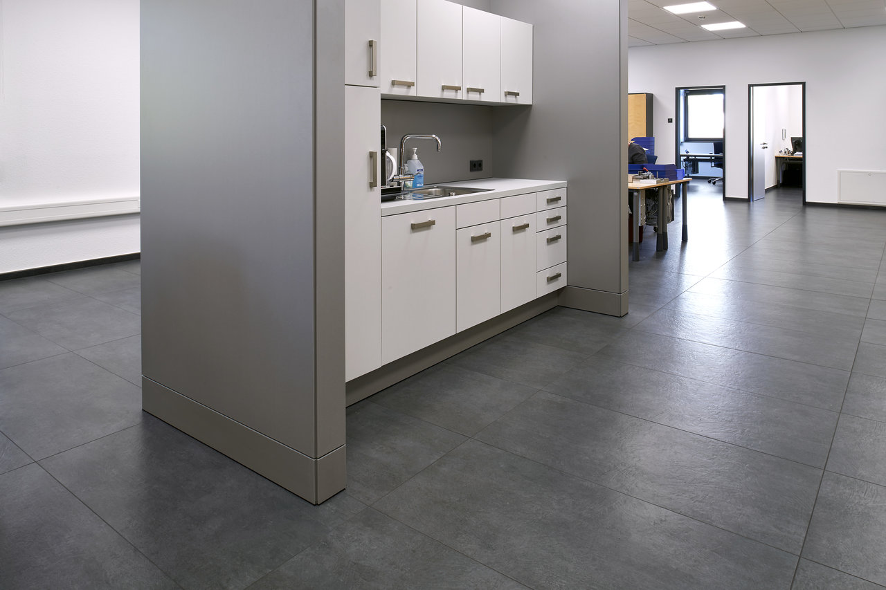 High-quality dark grey floor tiles in a modern office area with a kitchenette.