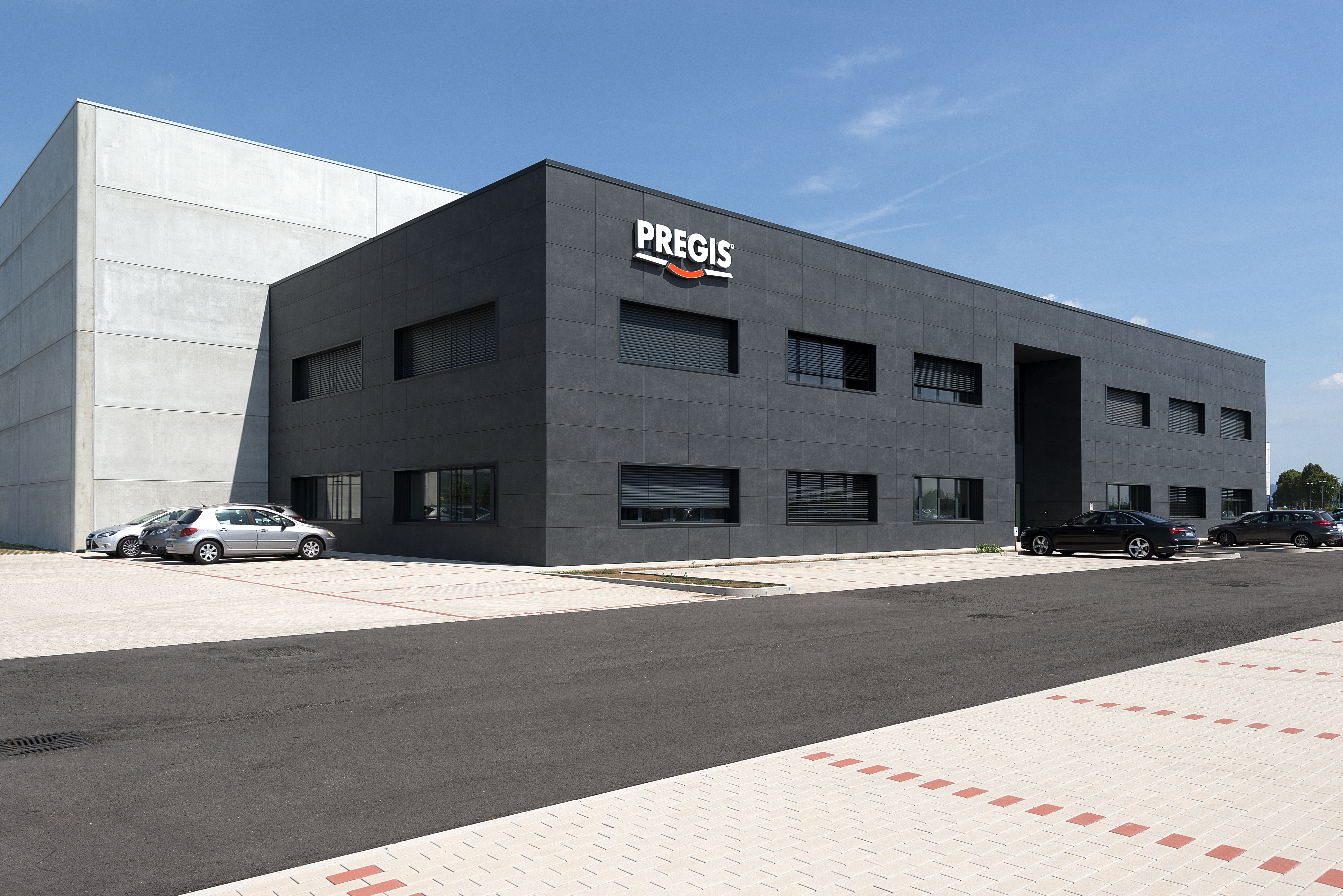 Modern office building by PREGIS with adjoining warehouse and parking spaces.
