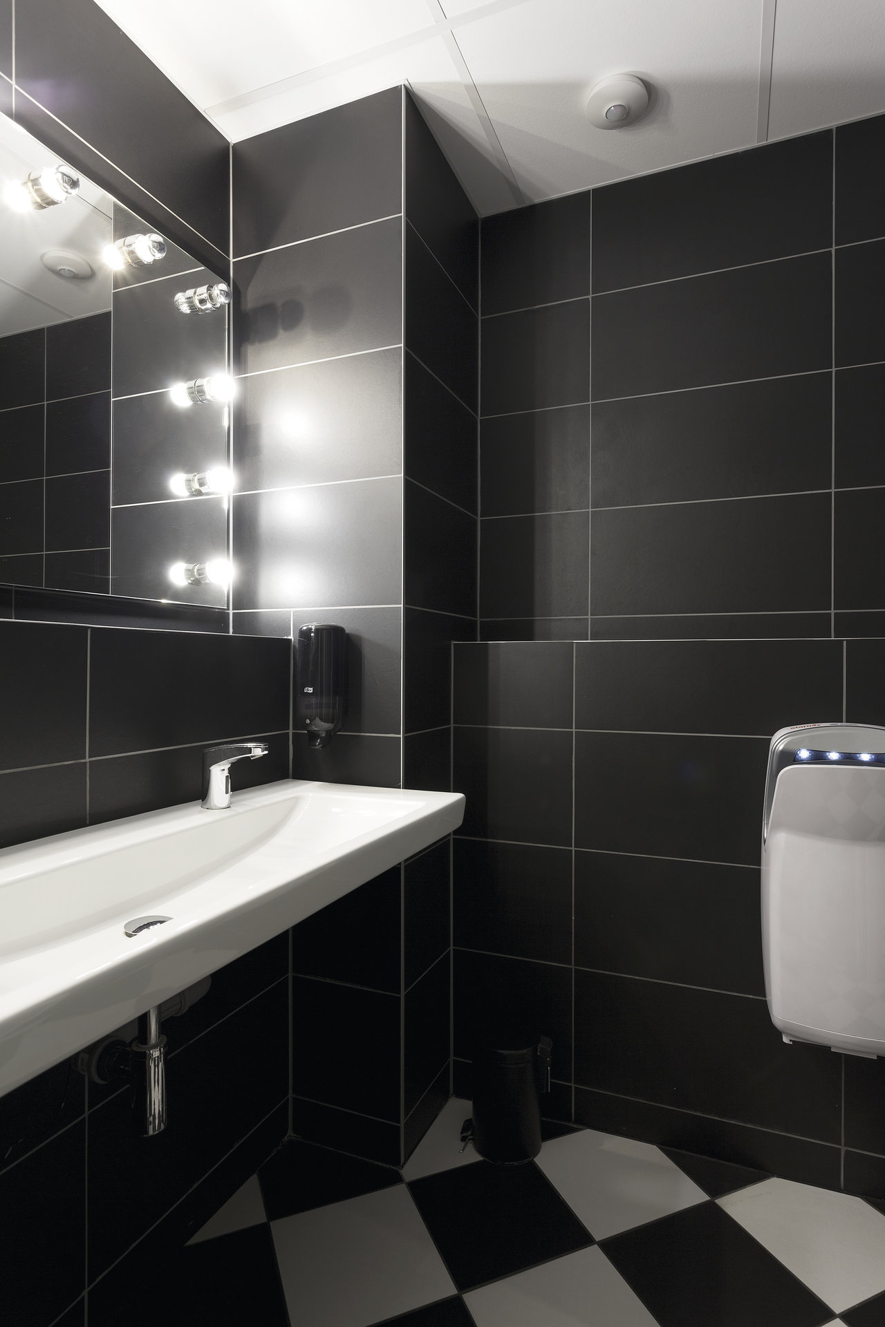 Bathroom with large-format black wall tiles and black and white floor tiles.