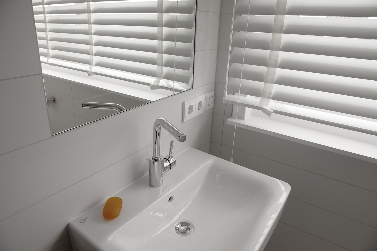 White tiled bathroom with modern washbasin, chrome tap and mirror.