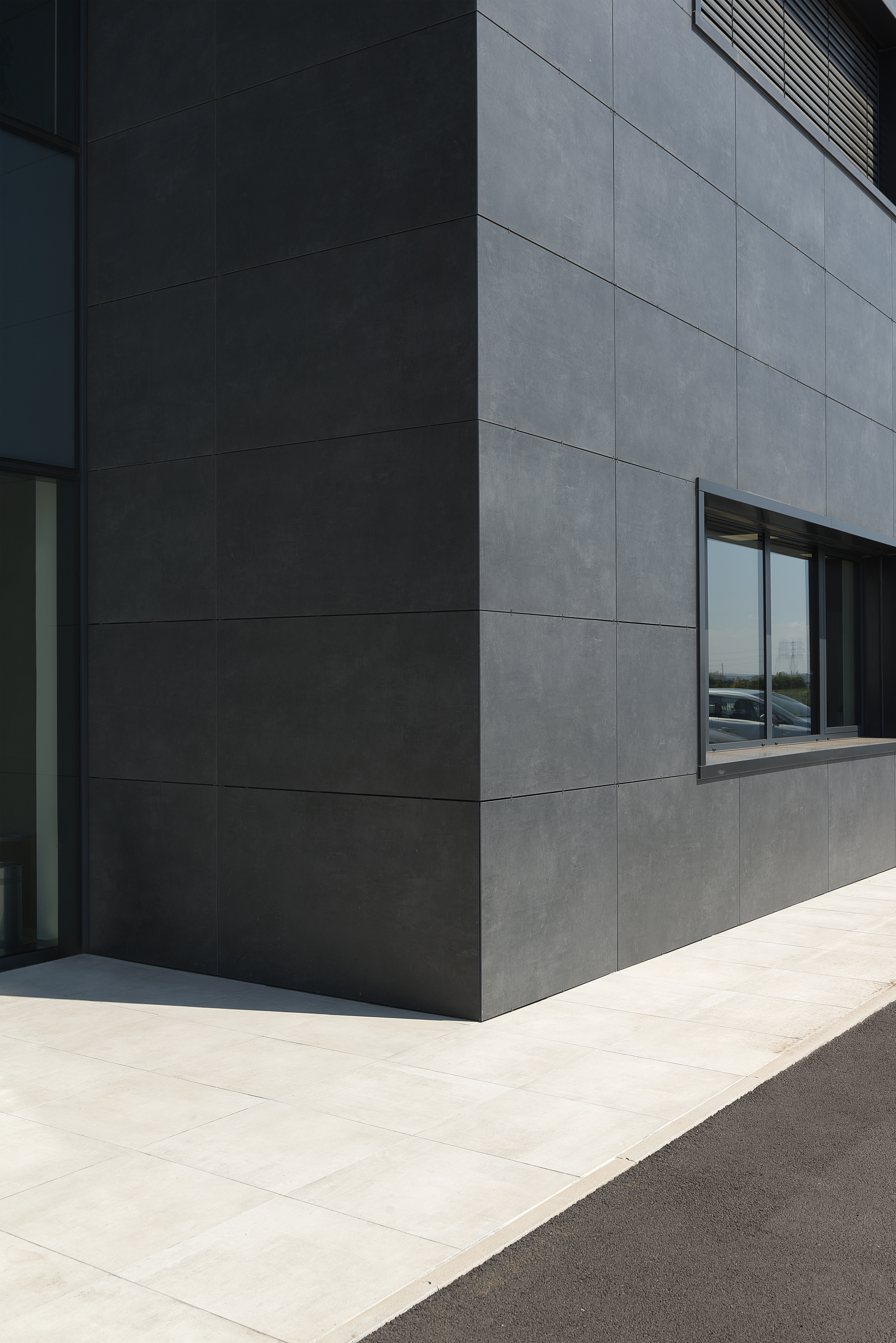 Dark facade tiles and light outdoor floor tiles on the corner of a modern building.