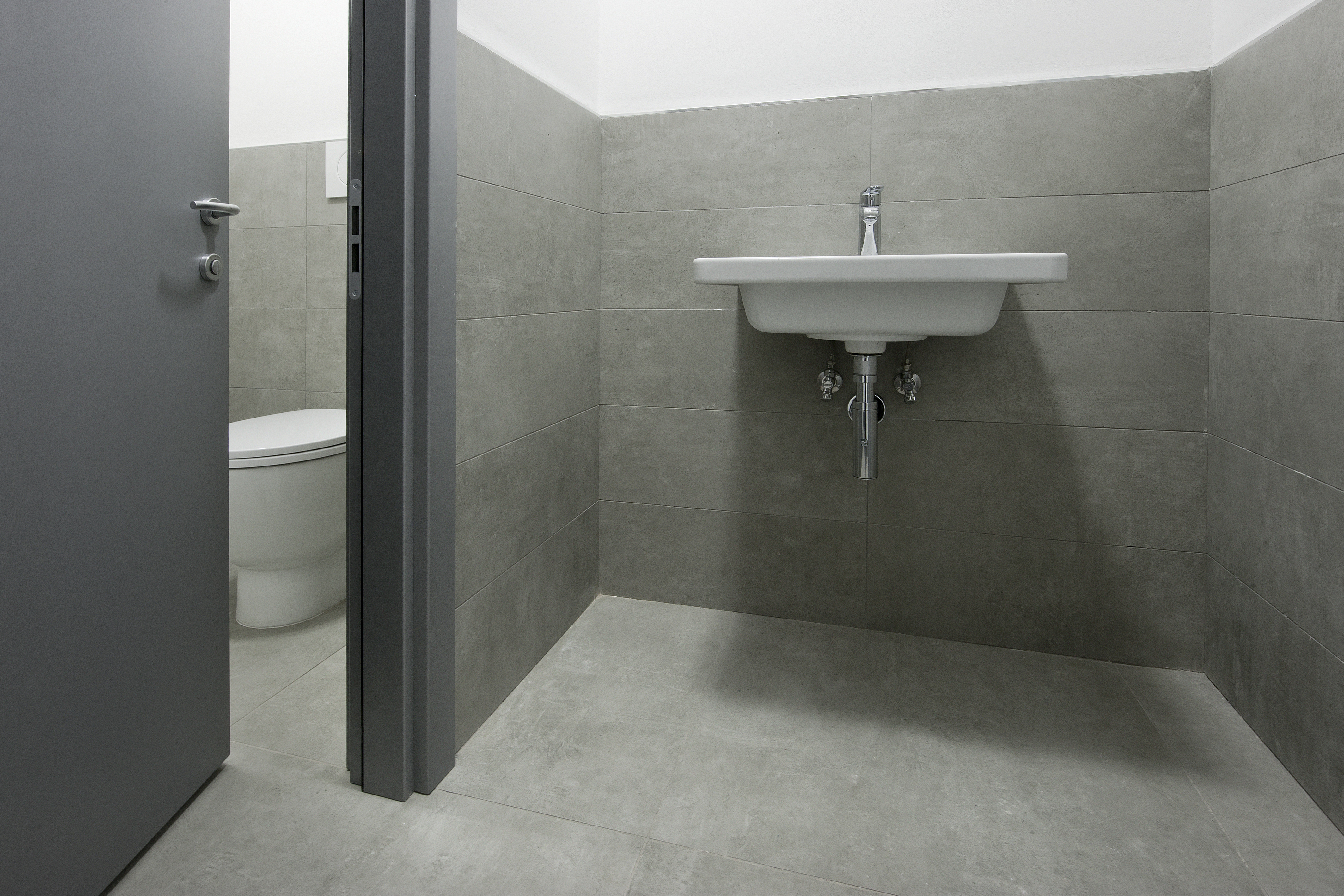 Modern bathroom with light grey concrete-effect floor and wall tiles, washbasin.