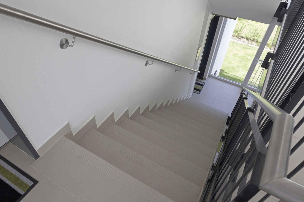 Straight staircase with light tile steps and modern stainless steel railing.