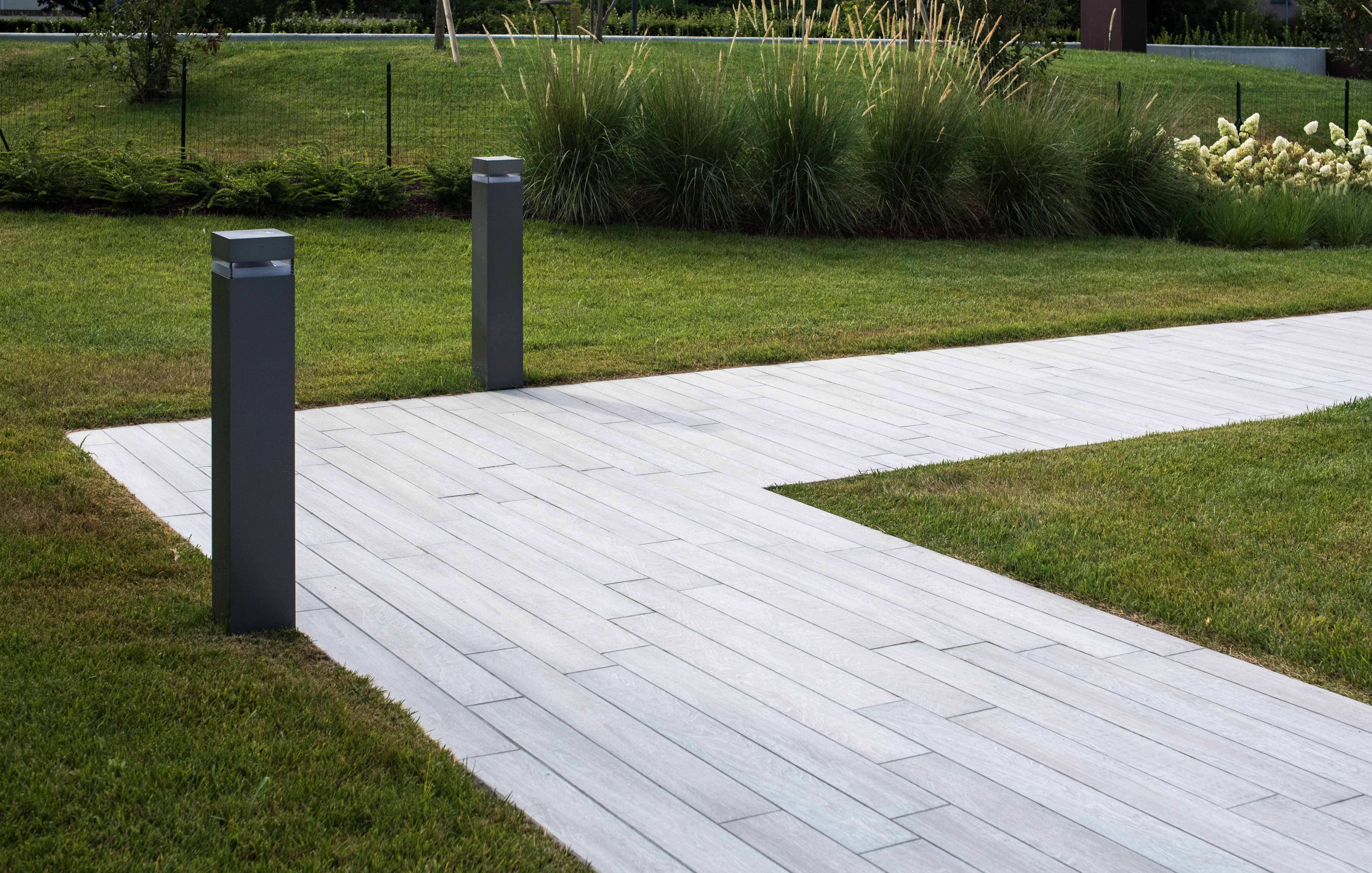 Outdoor wood-look tile path with lawn and lighting.