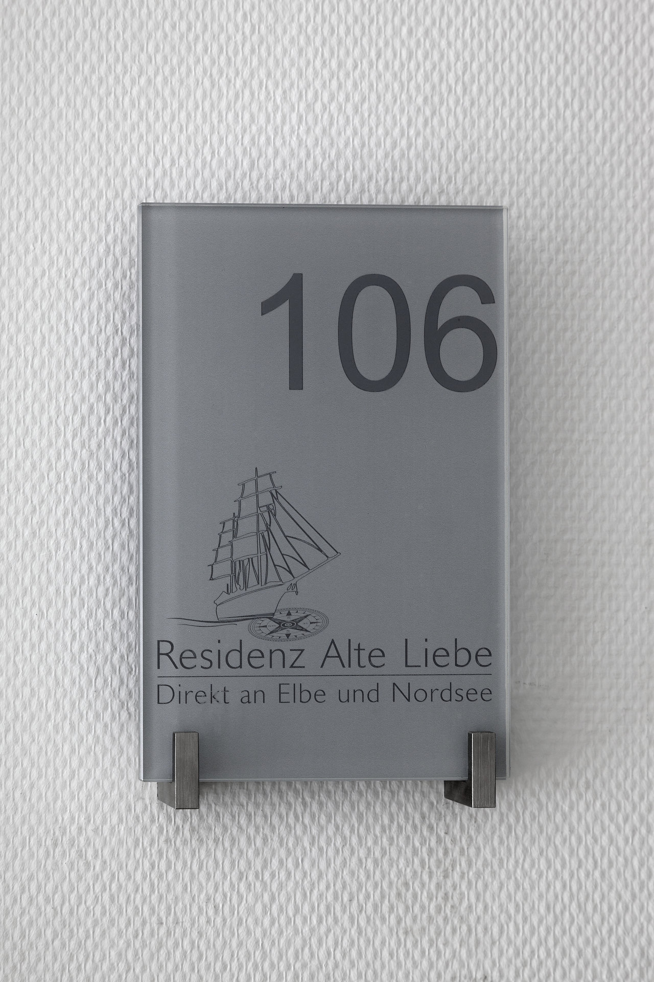 Grey glass sign with room number 106, sailing ship motif and "Residenz Alte Liebe".