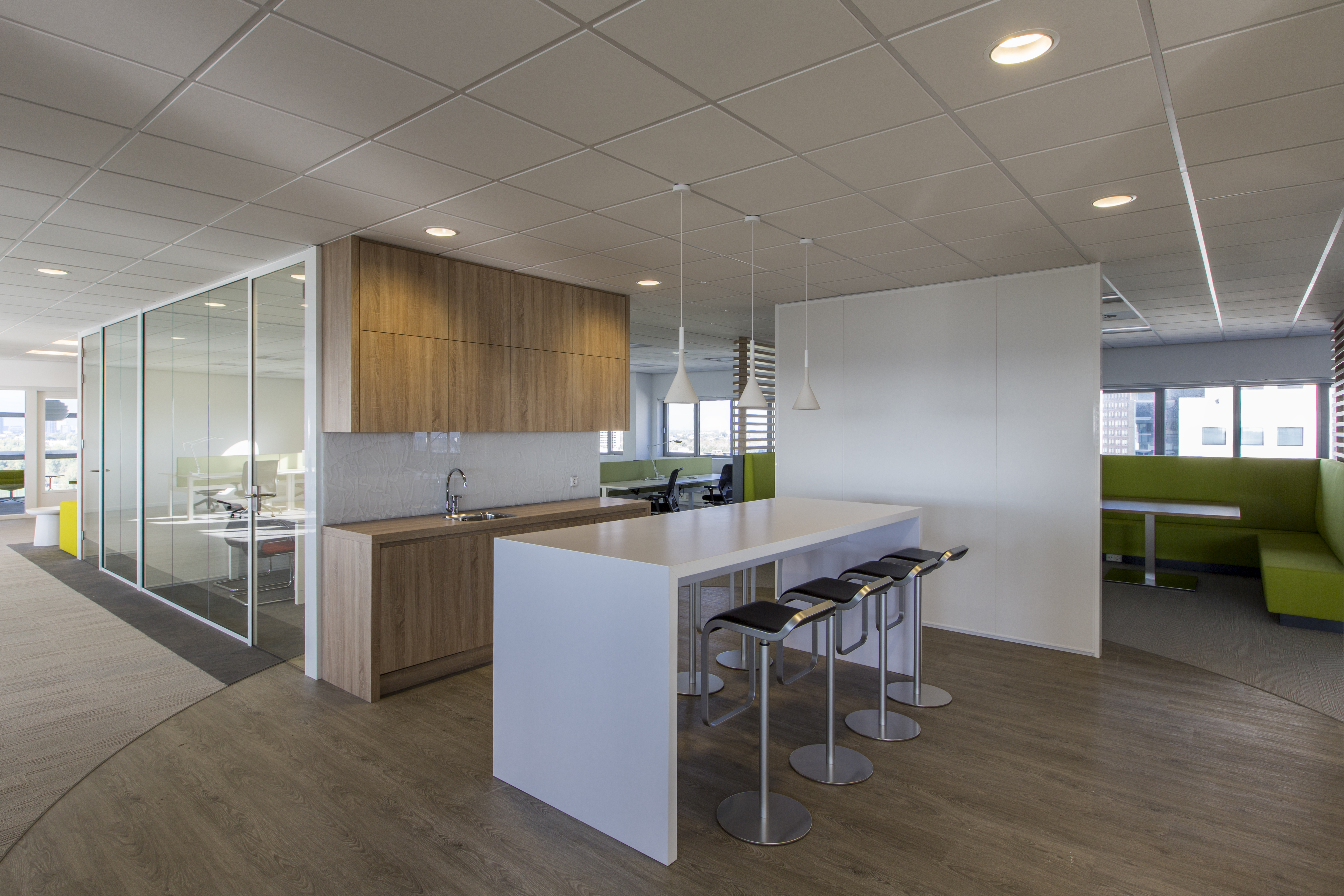 Modern office with light wood-effect tiles, kitchenette and seating.