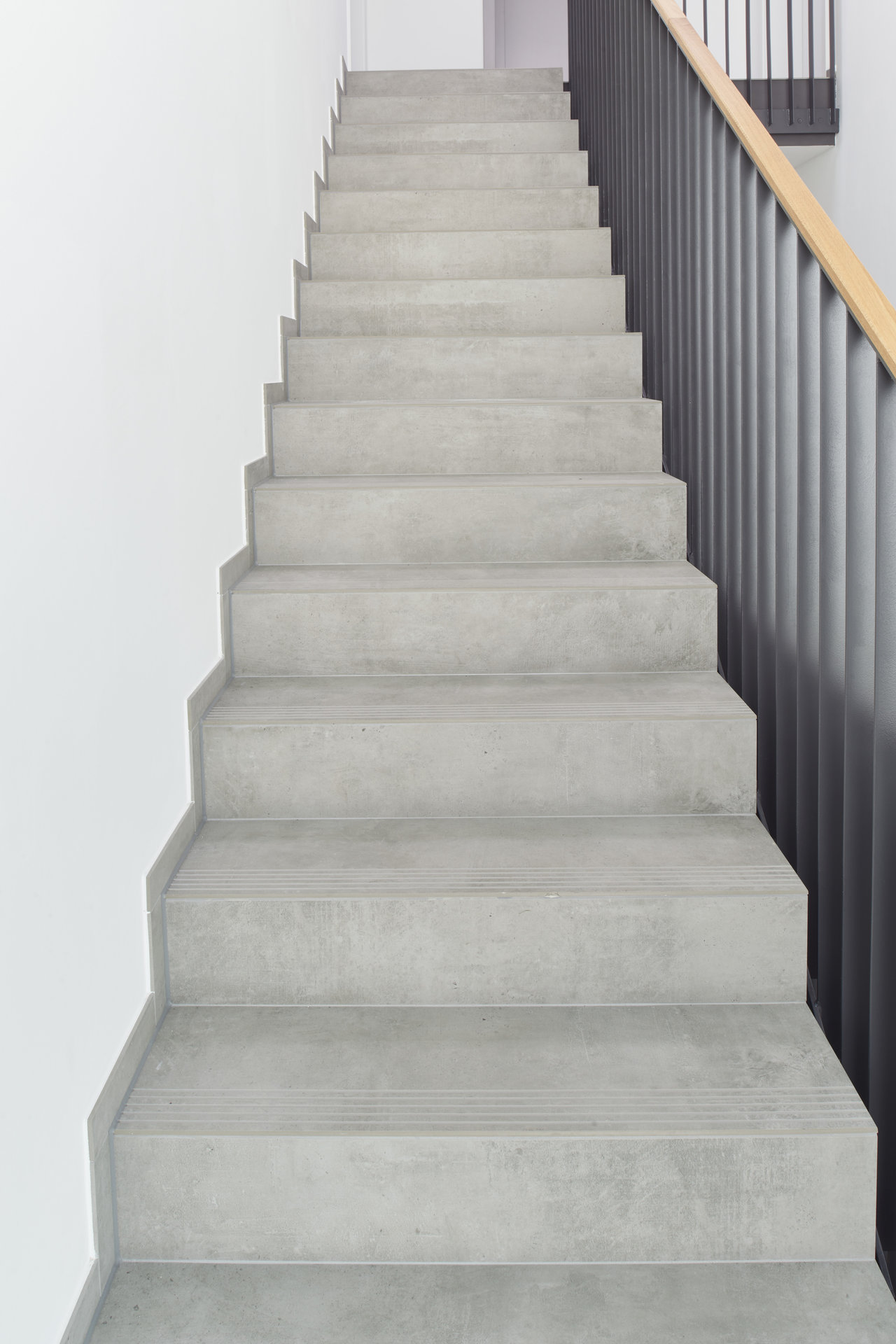Stairs with light grey concrete-look tiles and black railing.