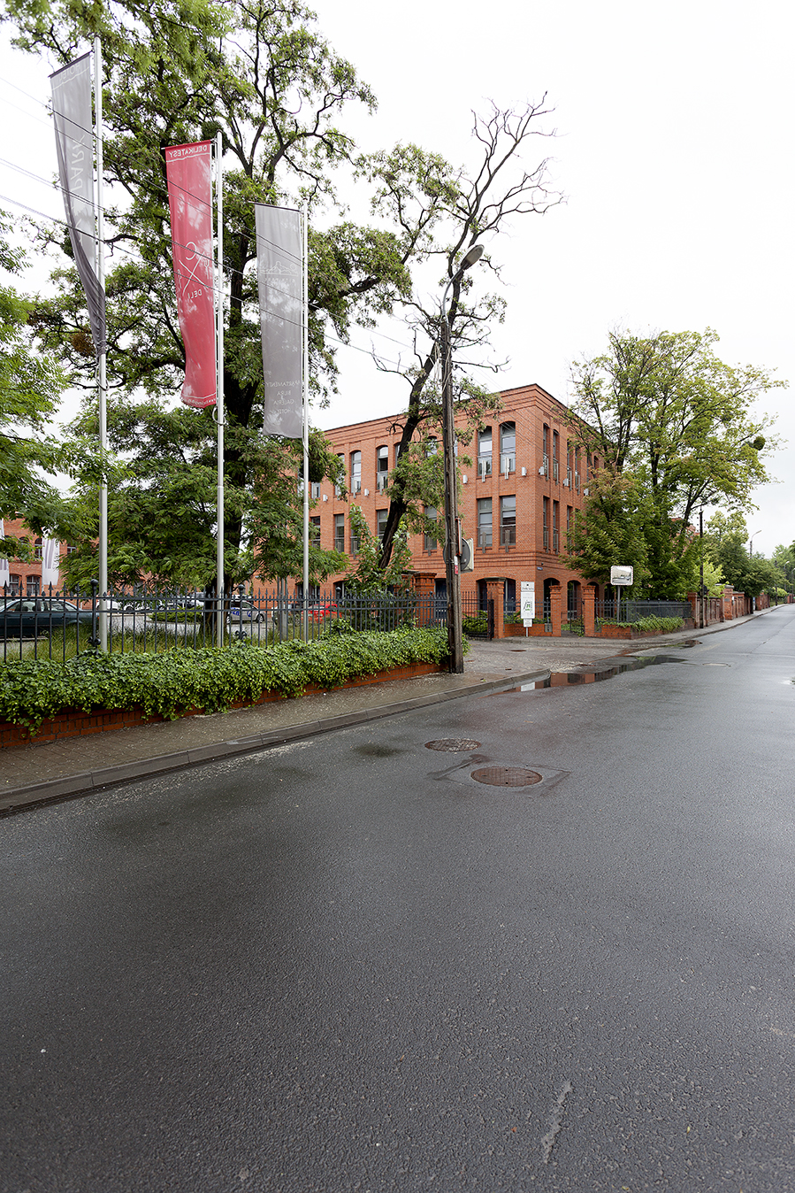 Brick building with flags and trees on a wet street.