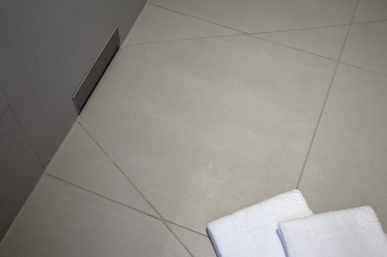 High-quality light grey floor tiles with modern grout and shower channel.