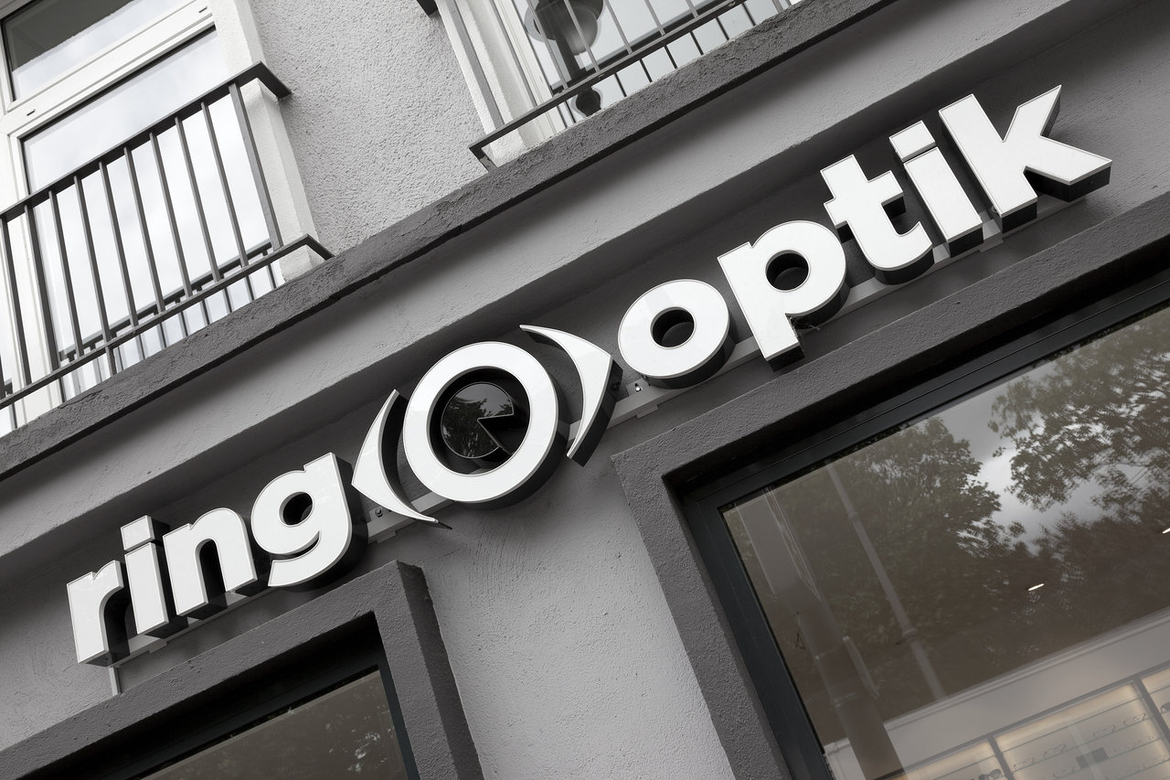 Illuminated 'ring look' sign with stylized eye as 'o' on building facade.