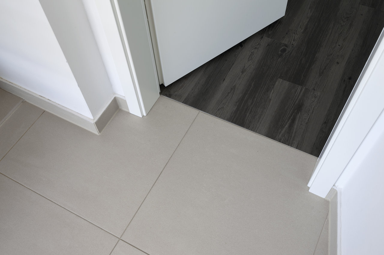 Light floor tiles and dark wood-look flooring at a threshold.