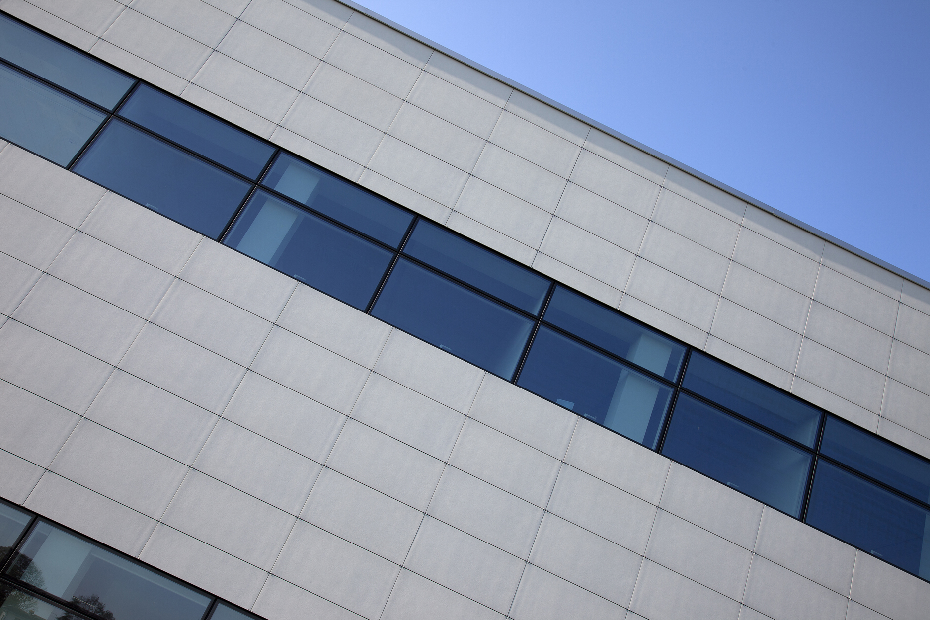 Light facade panels with a window band against a blue sky.
