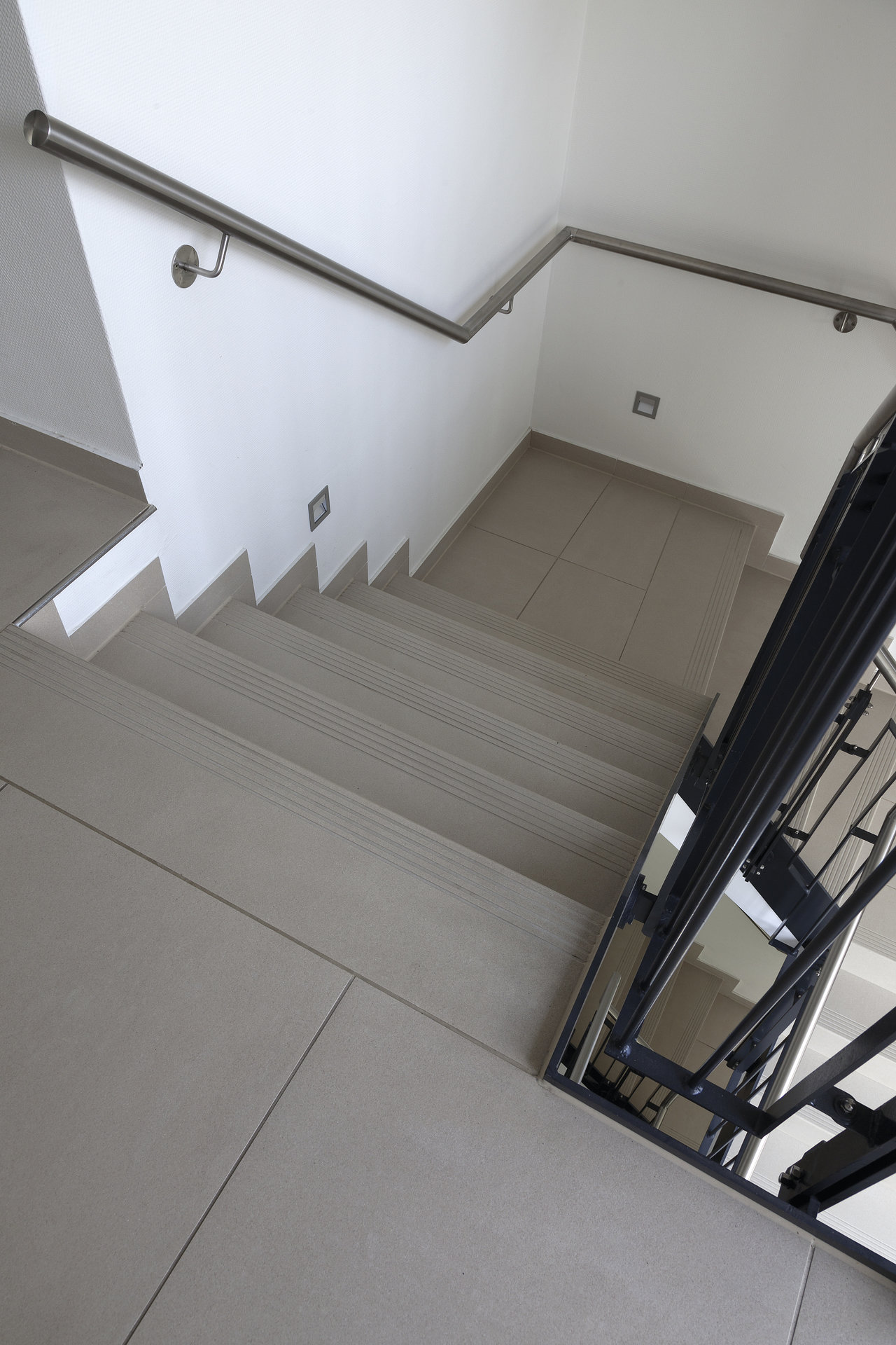 Modern staircase with light porcelain stoneware tiles and stainless steel railing.