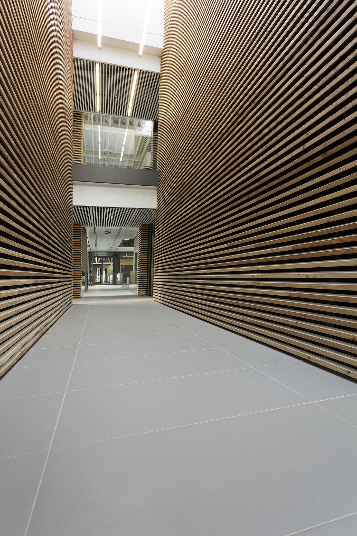 Modern hallway with large-format, light grey floor tiles and elegant wooden slatted walls.