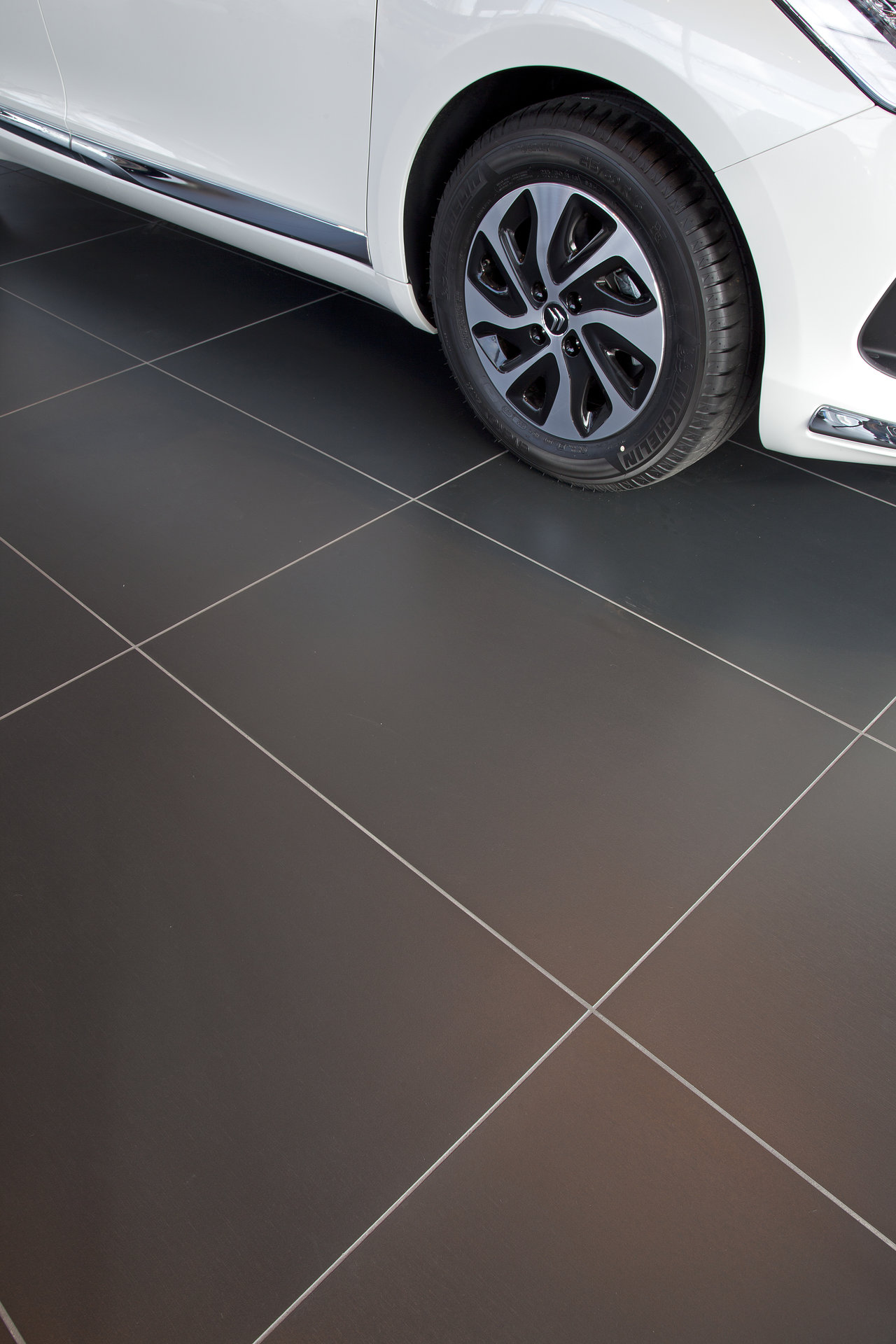 Premium dark grey floor tiles with fine grout, partly under a car.