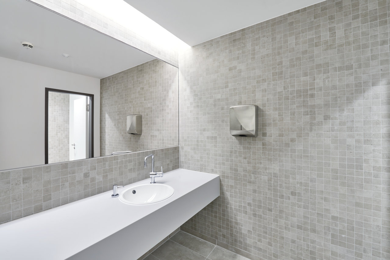 Modern bathroom with light grey mosaic tiles on wall and floor, white vanity and mirror.
