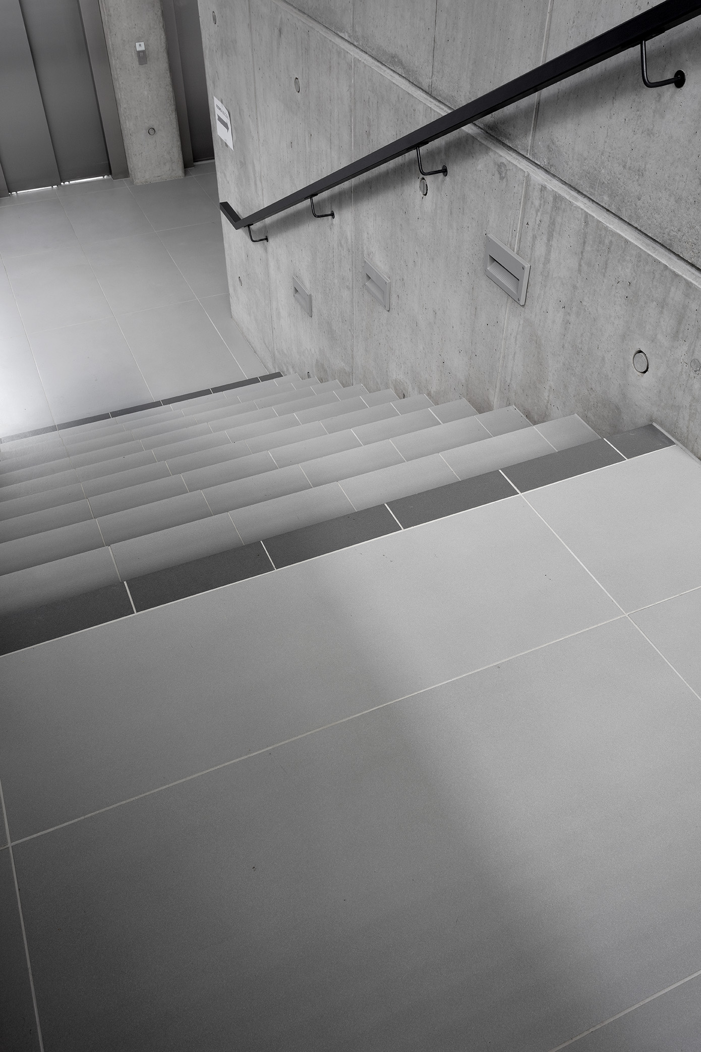 High-quality, large-format light grey tiles on a modern staircase with a concrete wall.