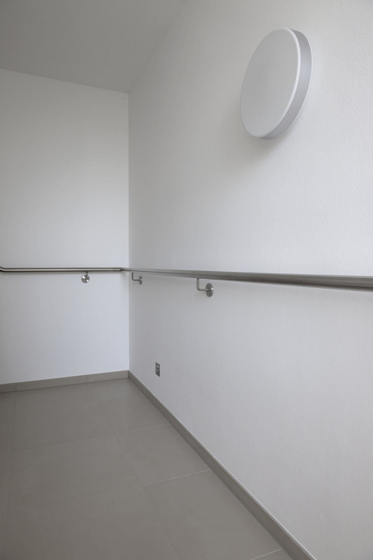 Modern room with light grey floor tiles, white walls, and a stainless steel handrail.
