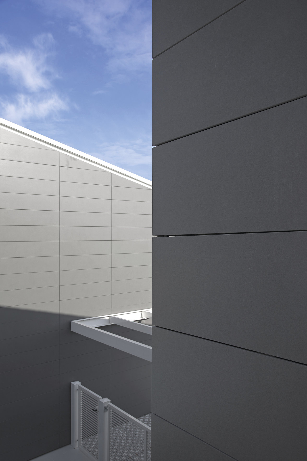 Modern facade with large-format grey outdoor tiles under a blue sky.