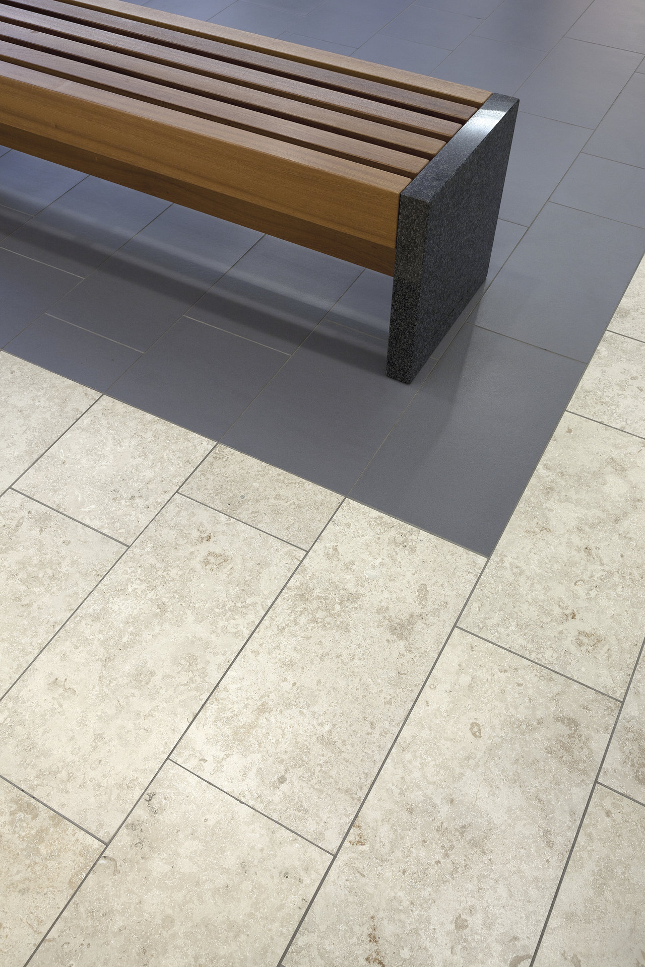 Light natural stone effect tiles and dark accent tiles under a modern wooden bench.