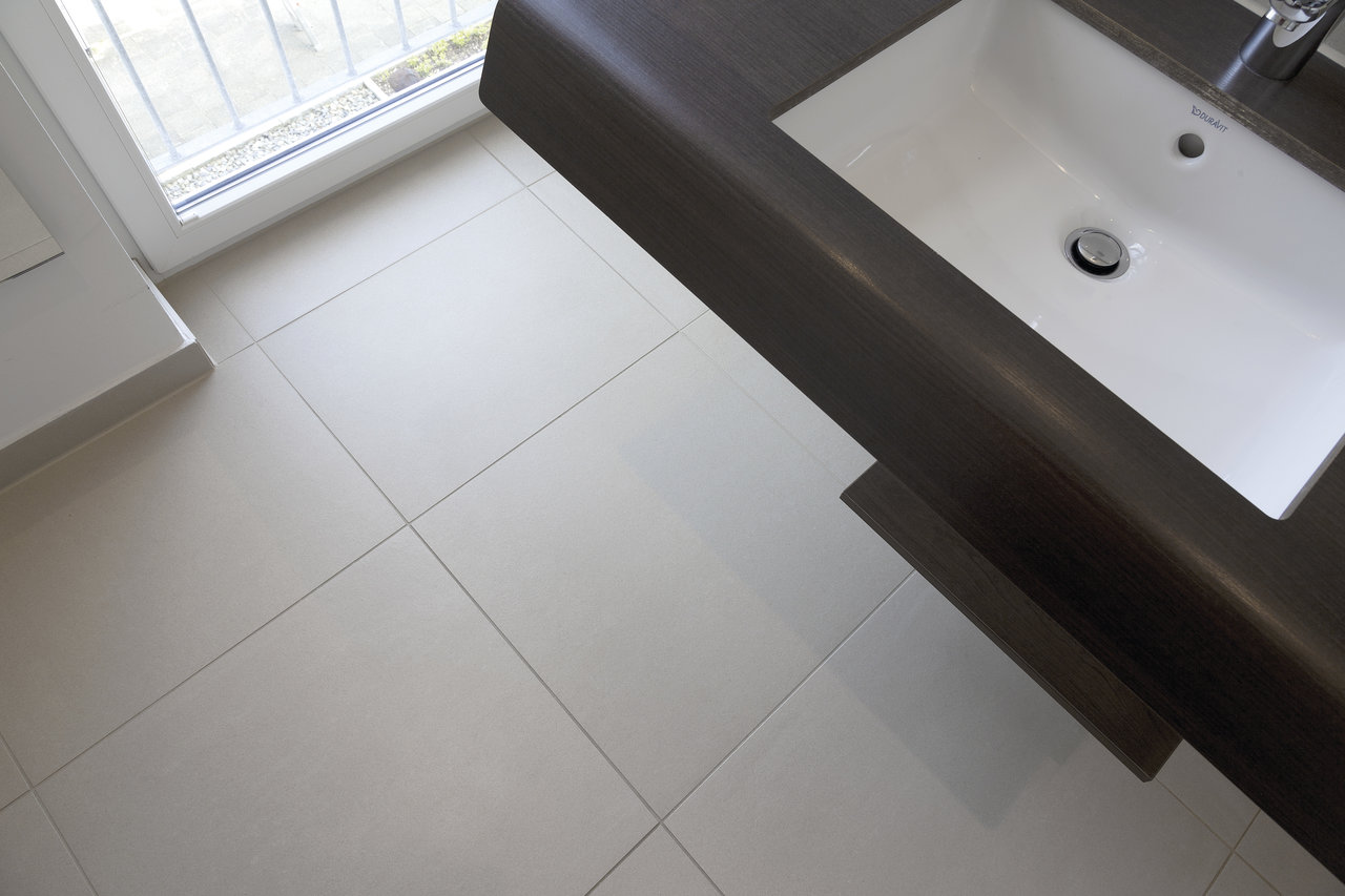 Bright, modern bathroom floor tiles next to a dark vanity unit.