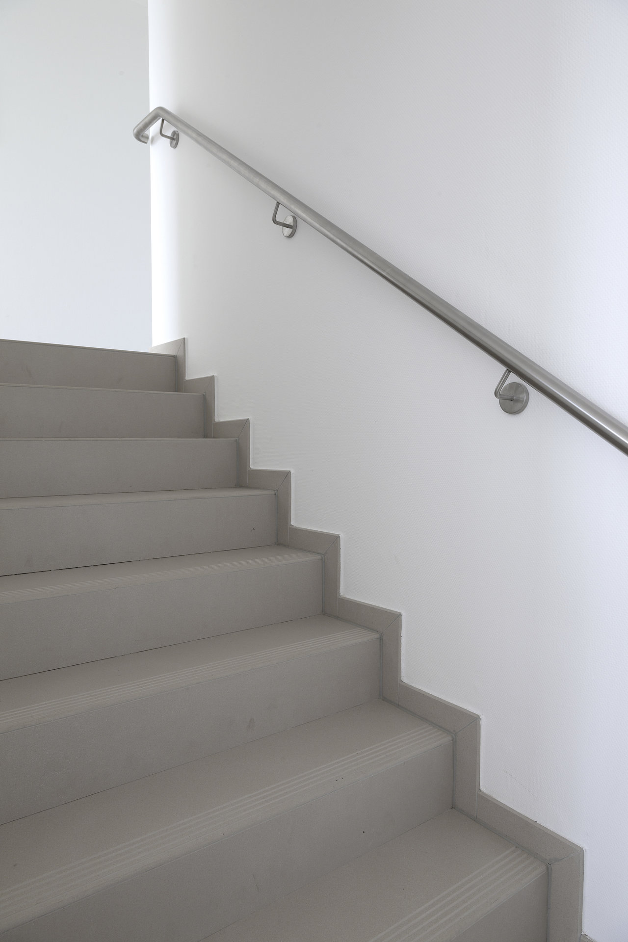 High-quality light grey tiles on a modern staircase with a stainless steel railing.