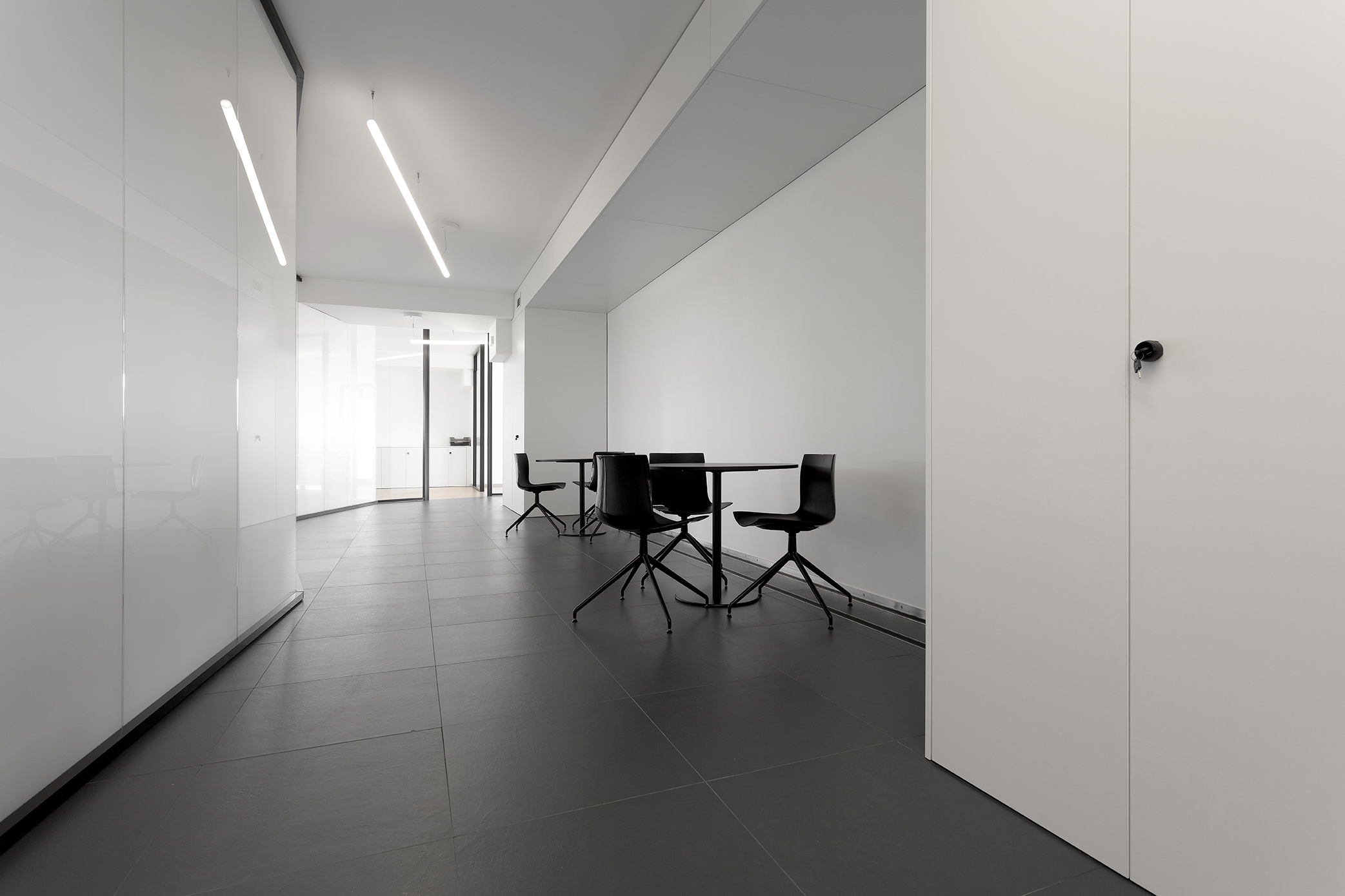 Modern interior with dark floor tiles, white walls, and black tables.