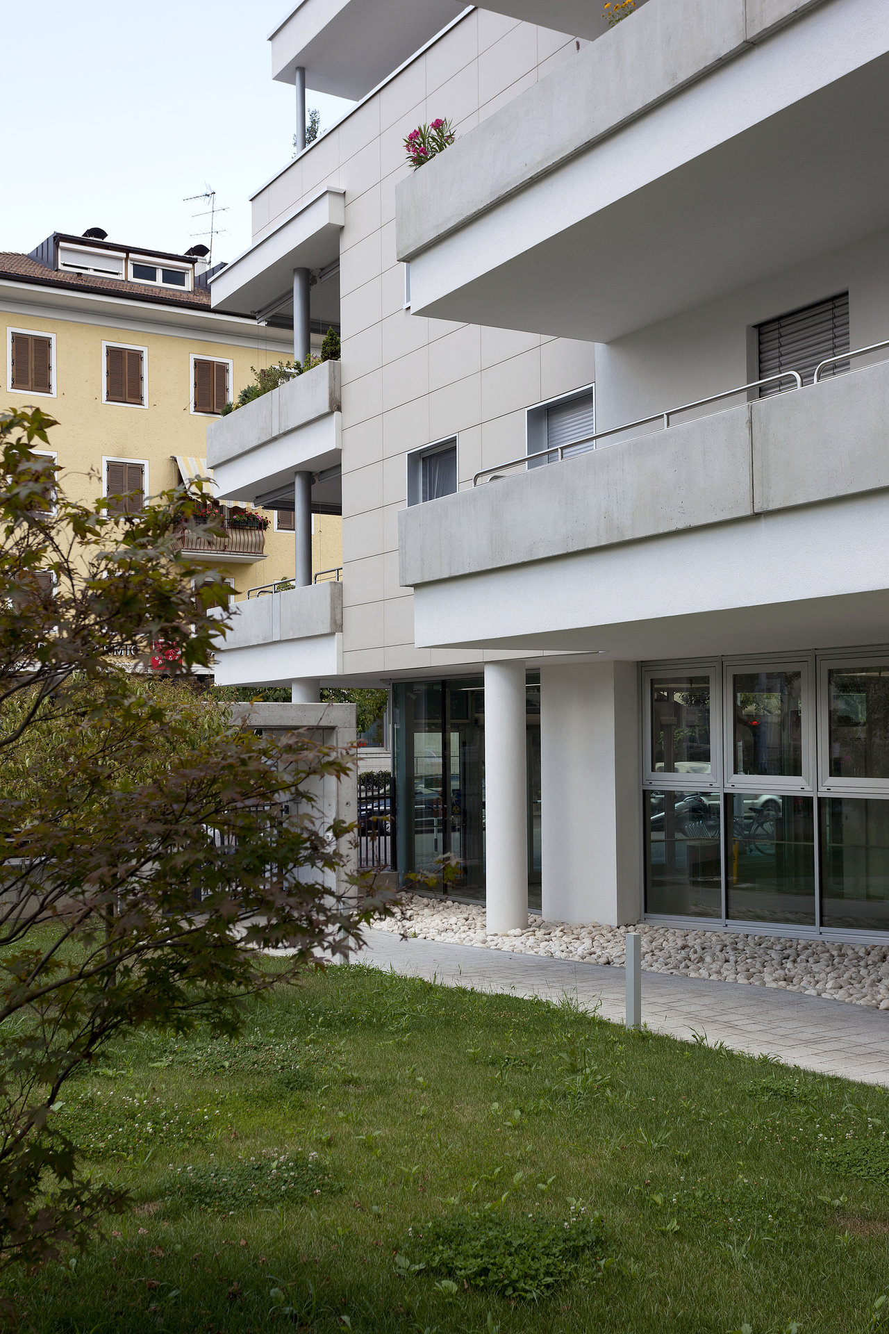 Contemporary building with balconies, light-coloured tiles on facade and path.