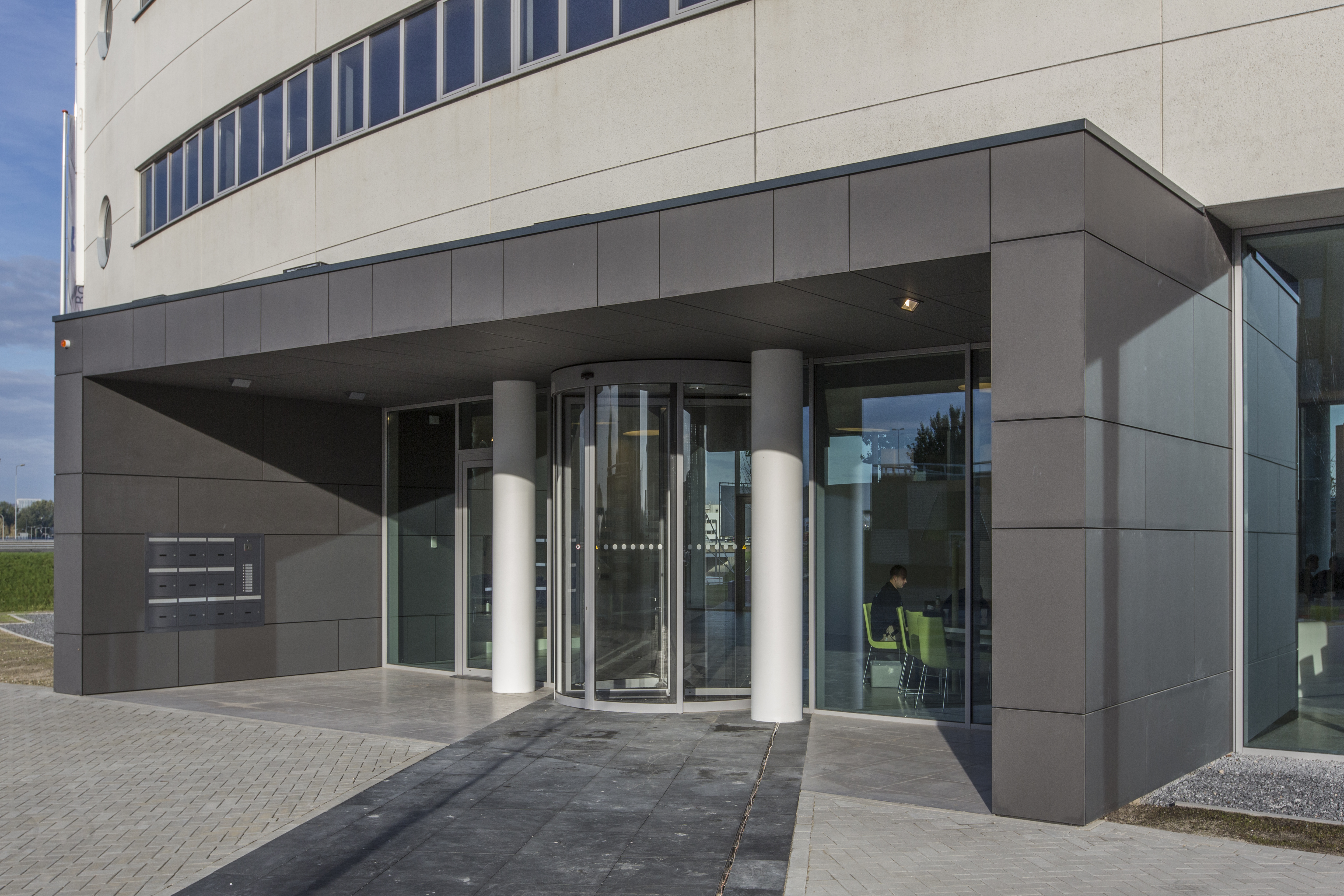 Modern building entrance with a glass revolving door and dark exterior tiles.