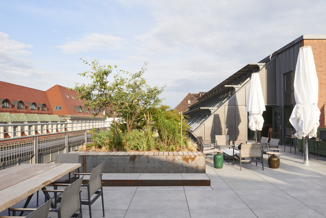 Modern roof terrace with light grey outdoor tiles, plants, and various seating areas.