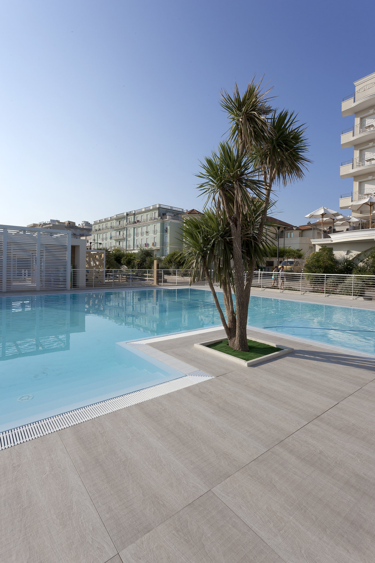 Light wood-effect outdoor tiles around a modern pool with a palm tree.