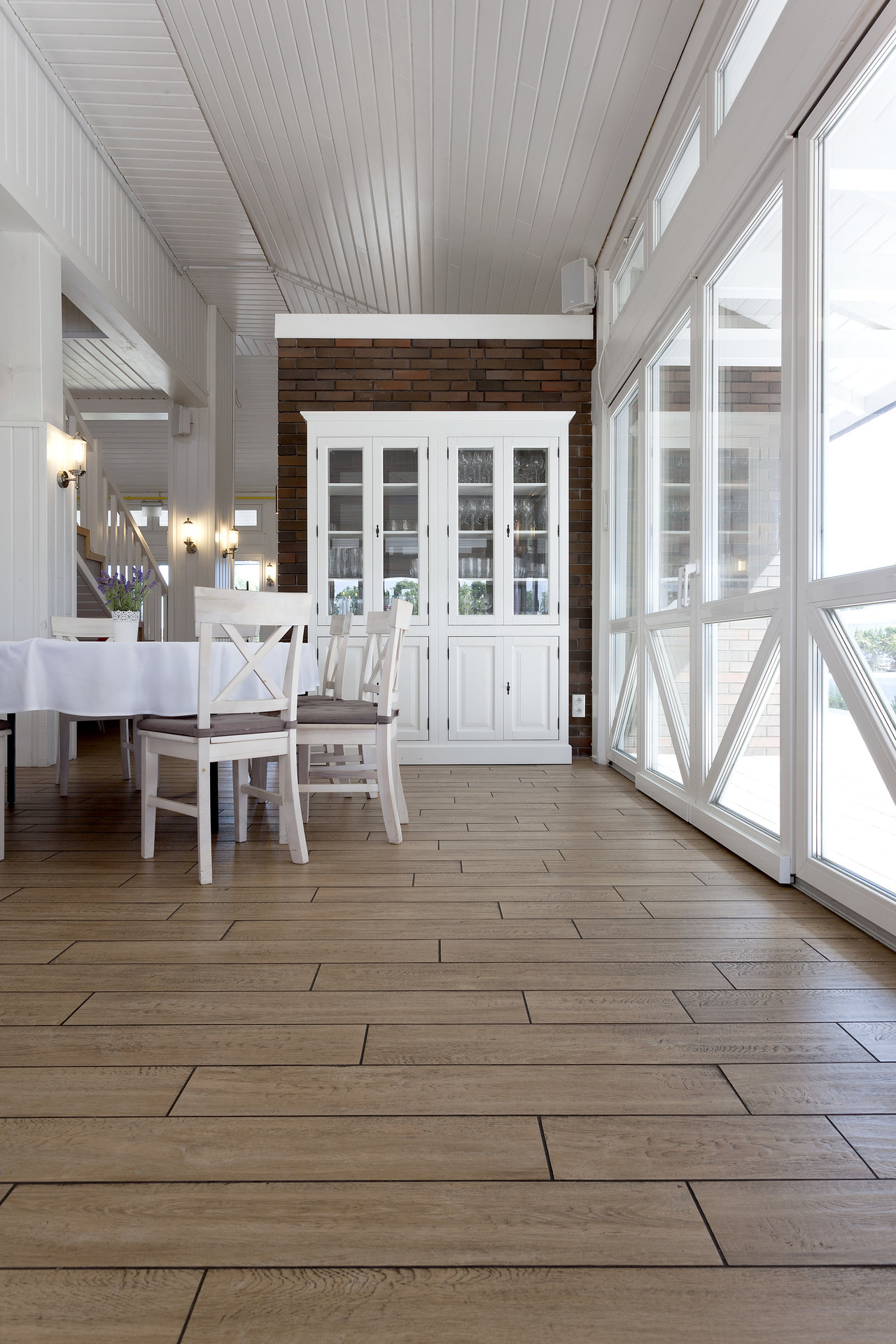 High-quality tiles with a warm wood effect in a bright dining area with white furniture.