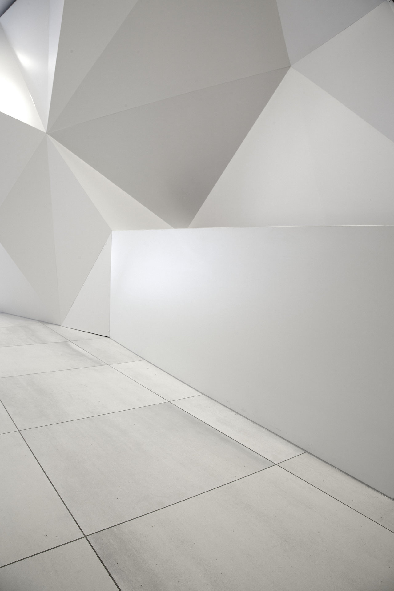 Light, large-format porcelain tiles on the floor of a modern room with a white, geometric wall.