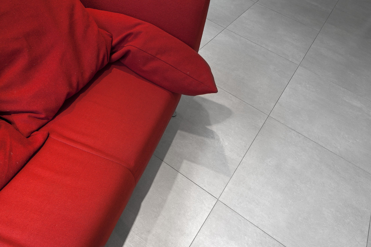 Modern grey concrete-effect floor tiles next to a red sofa.