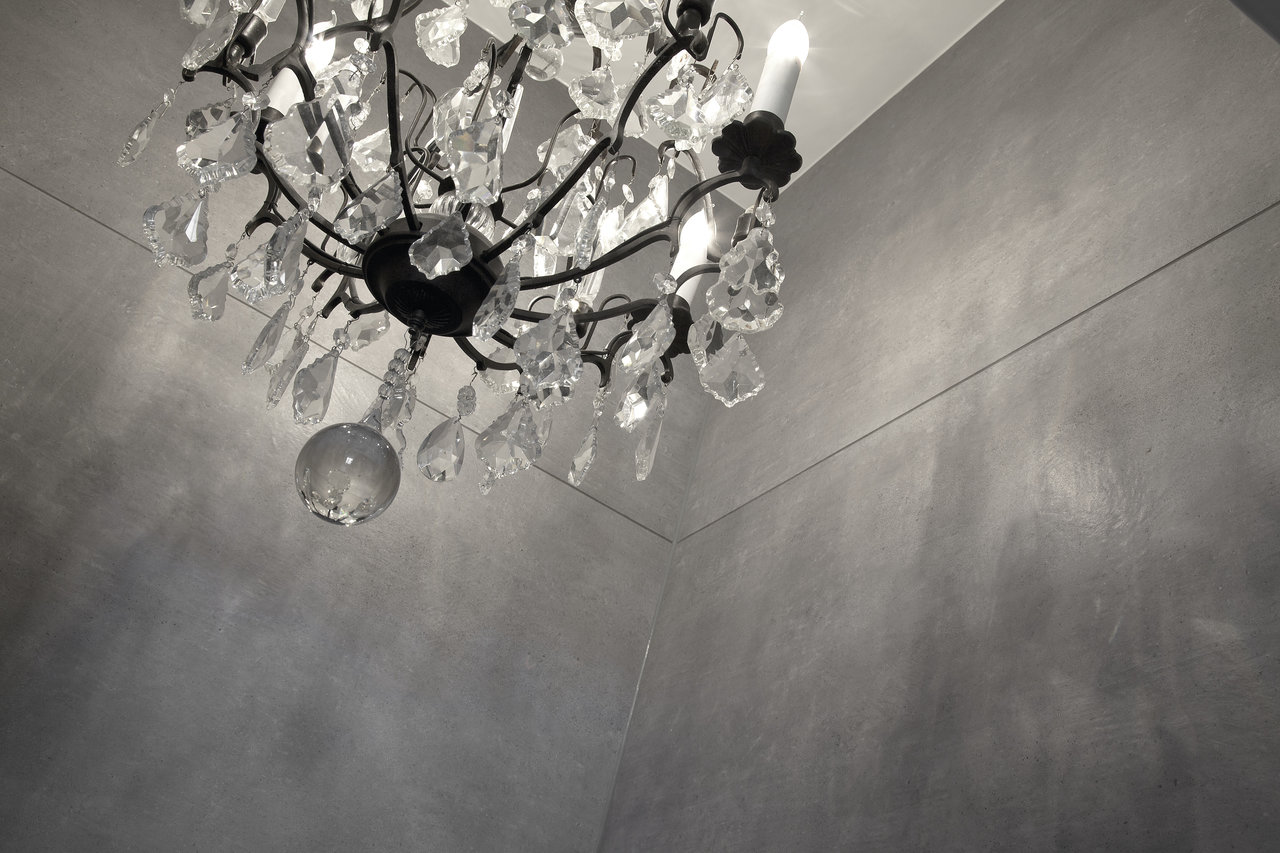 Crystal chandelier against a wall of elegant grey concrete-effect tiles.
