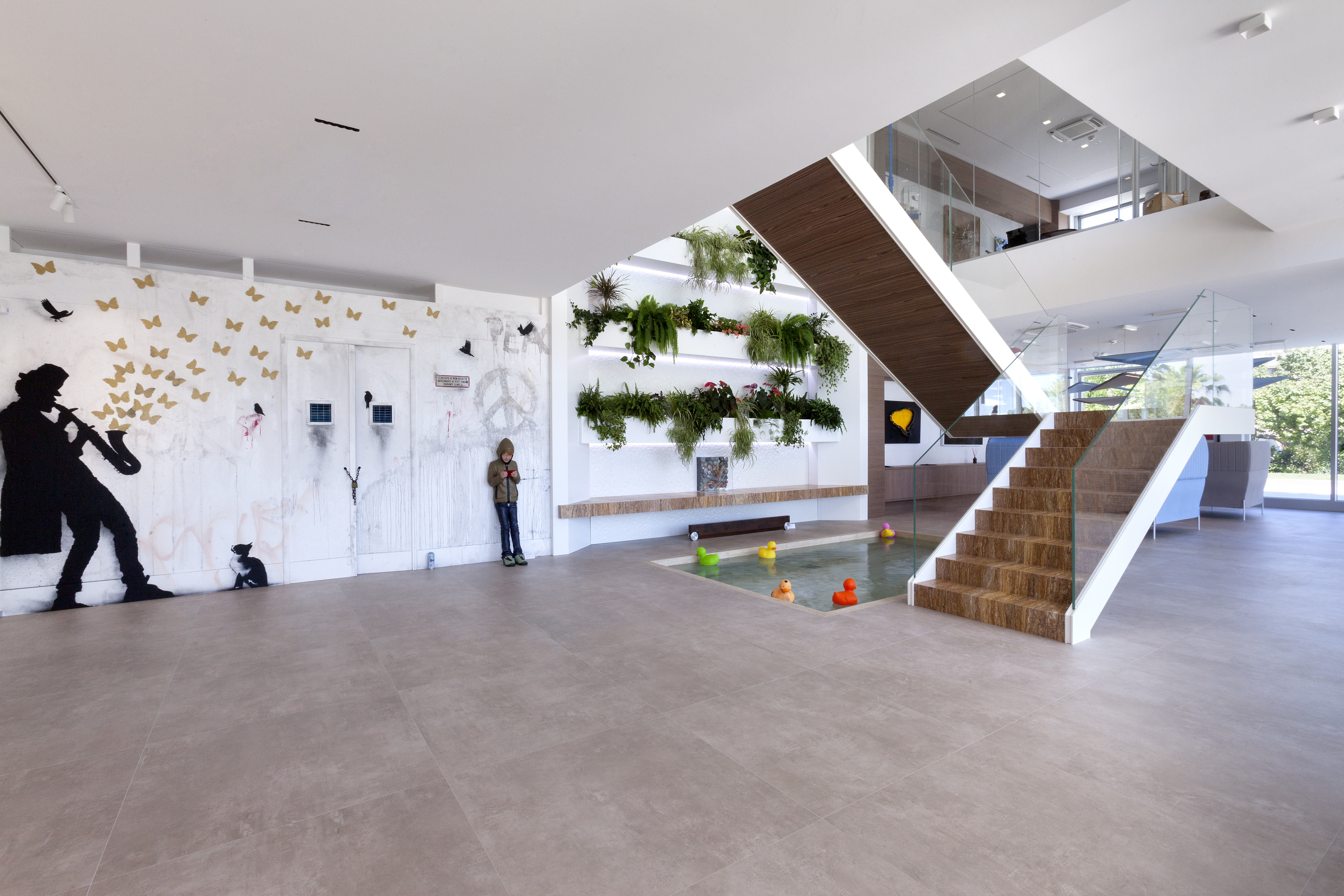 Modern Showroom with light floor tiles, elegant staircase, plant wall, and art.