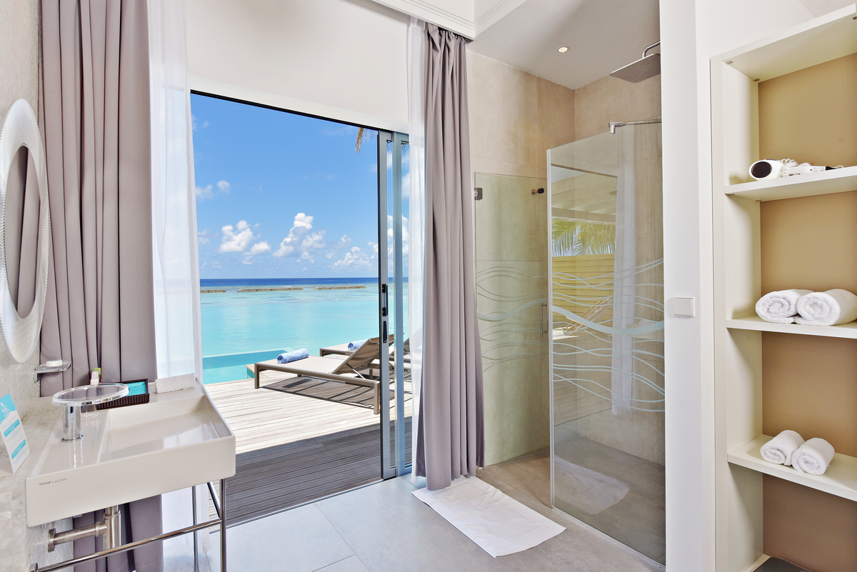 Light tiles in a modern bathroom with an open shower and direct access to the terrace with sea view.