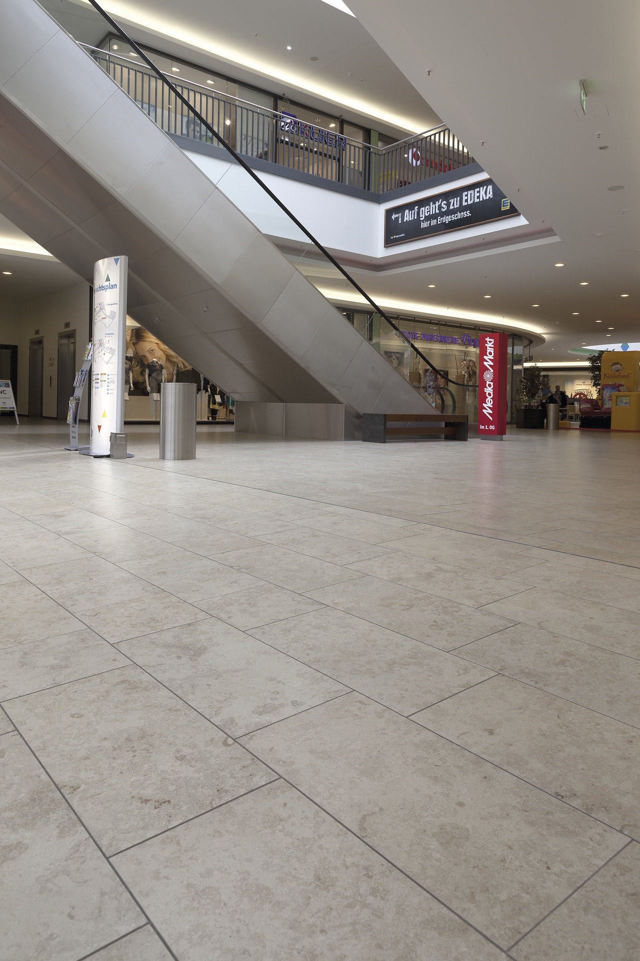 Bright, large-format tiles in a modern mall with escalator.