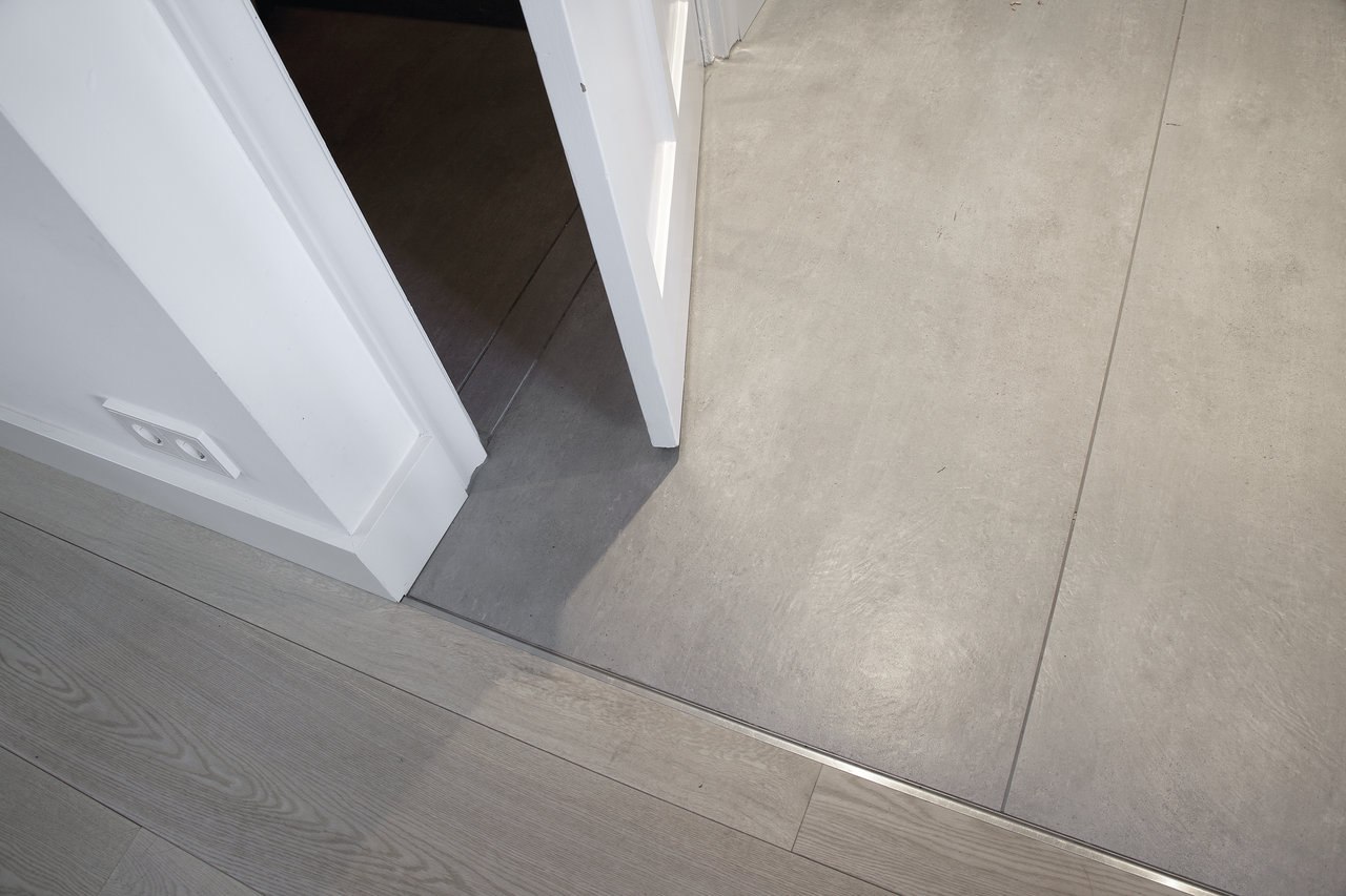 Transition from light grey wood-effect tiles to grey concrete-effect tiles.