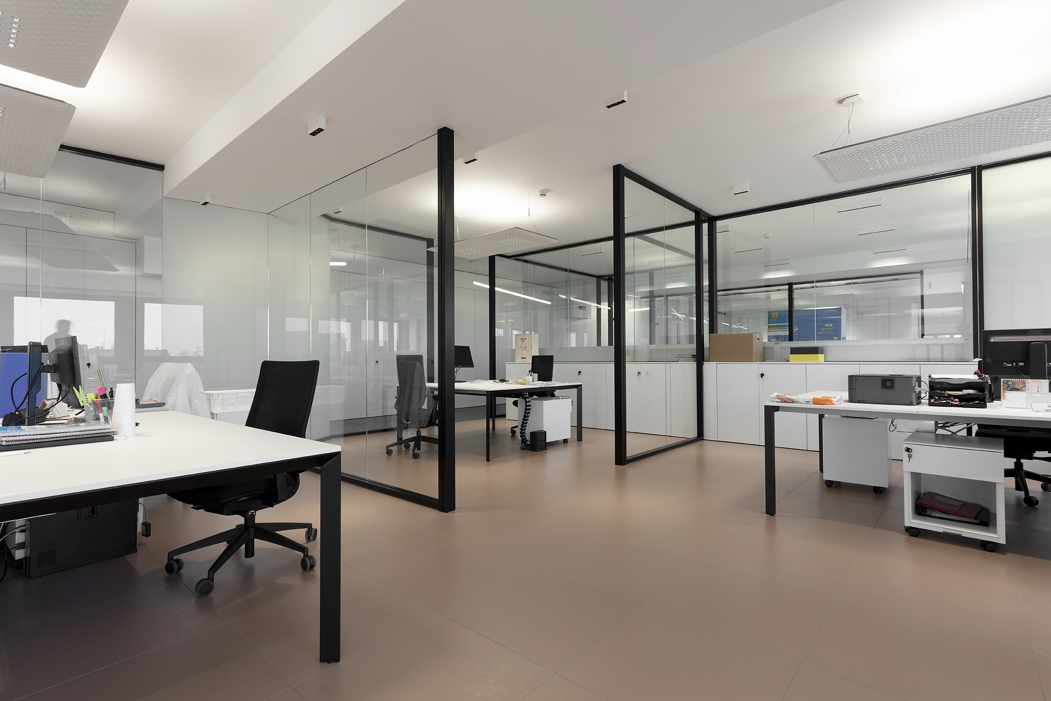 Modern office with large-format, light brown floor tiles and glass walls.