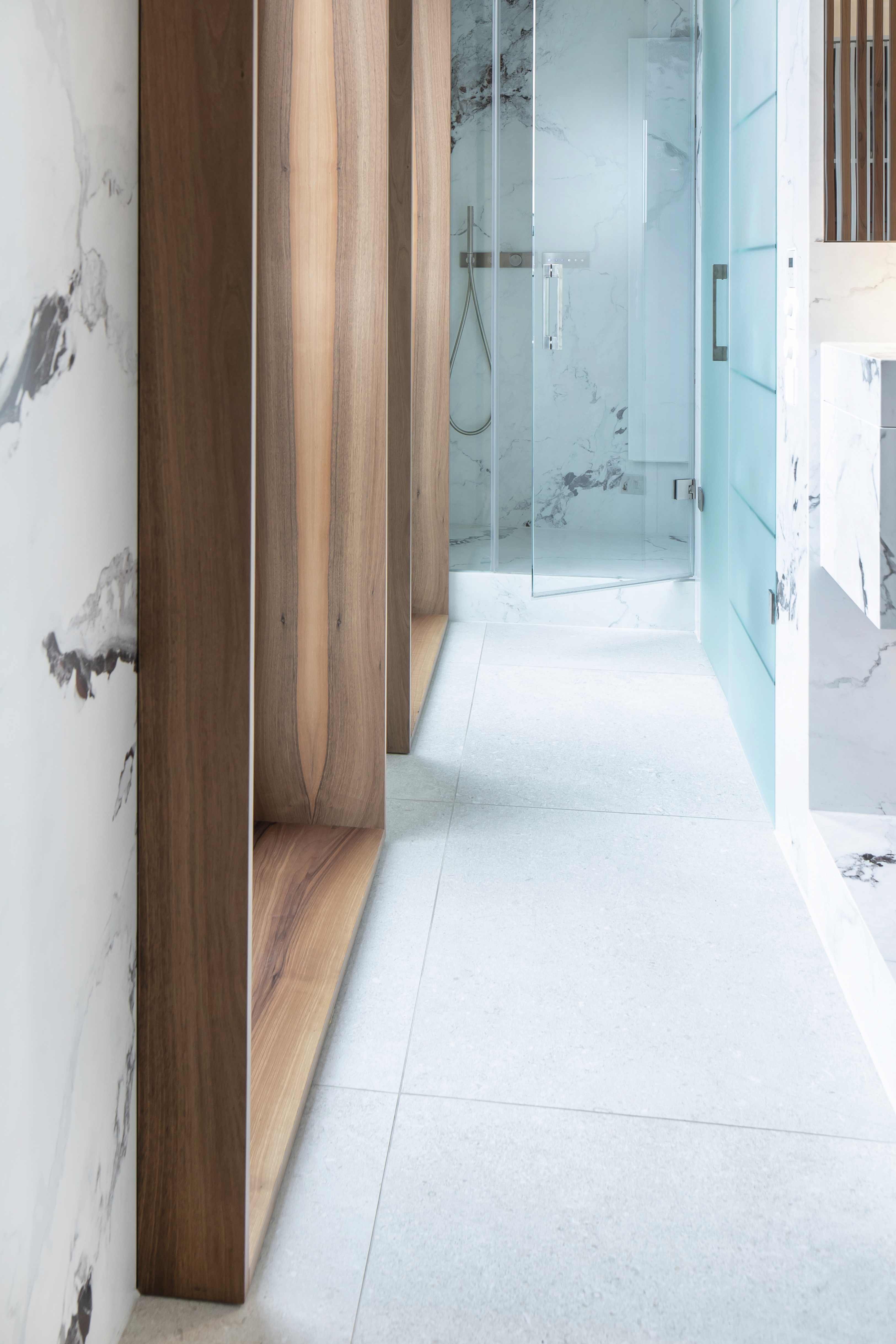 Modern bathroom with light floor tiles, marble-look wall tiles, and wooden elements.