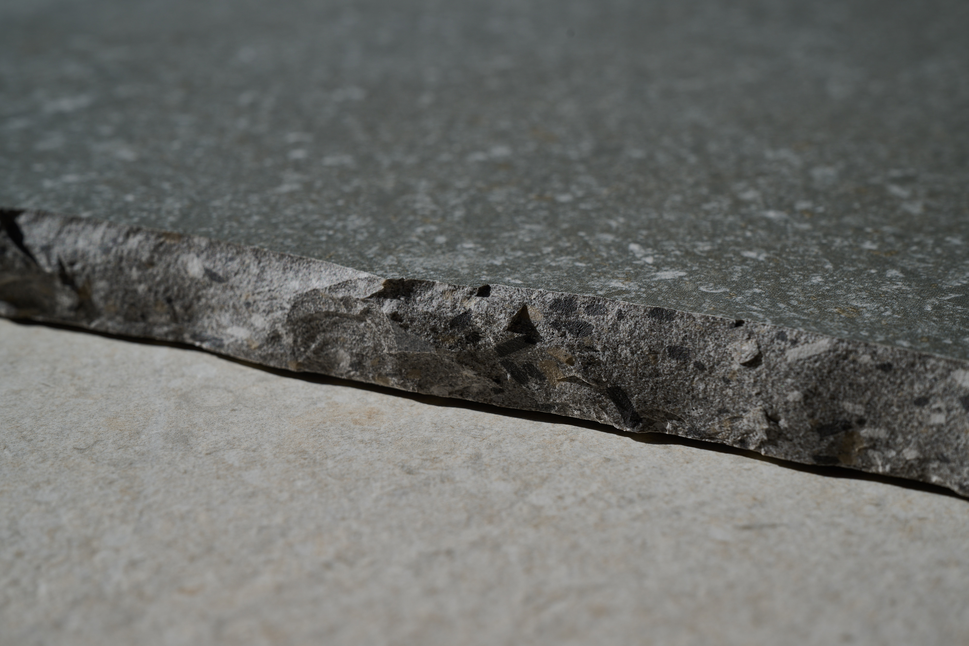 Rough-cut edge of an anthracite tile with a textured surface.