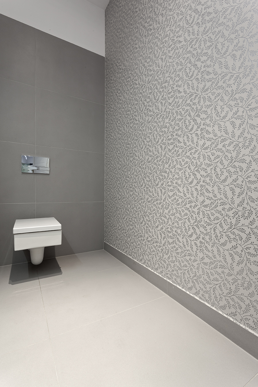 Modern WC with light grey floor tiles and two grey wall tiles, one with a leaf pattern.